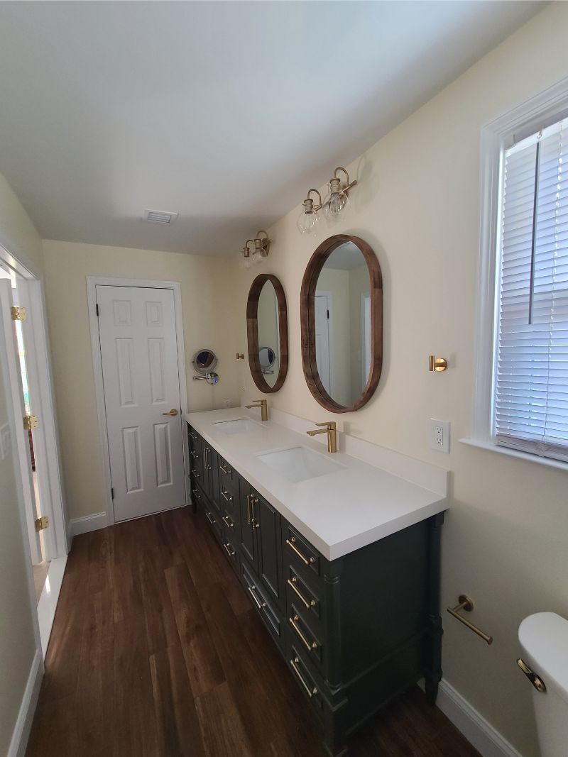 Bathroom with dark green double vanity, oval mirrors, and white countertops.