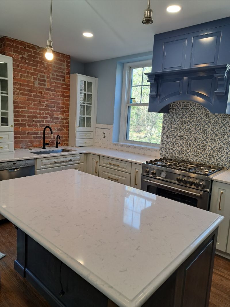 Modern kitchen with white island, brick wall, blue range hood, and light cabinets.