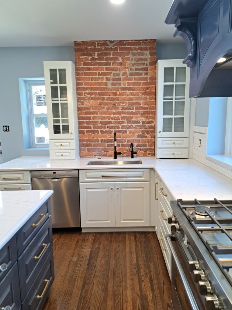 Modern kitchen with white cabinets, stainless steel appliances, brick wall, and dark wood floors.