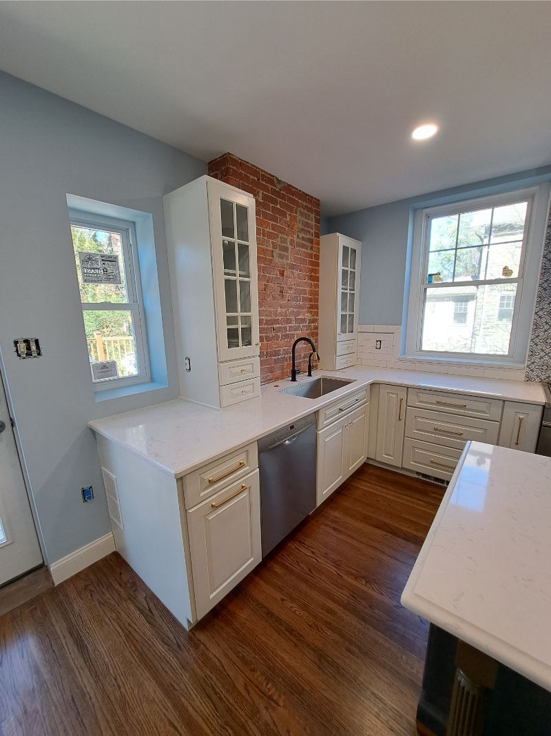A renovated kitchen with white cabinets, a brick wall, and dark wood floors.