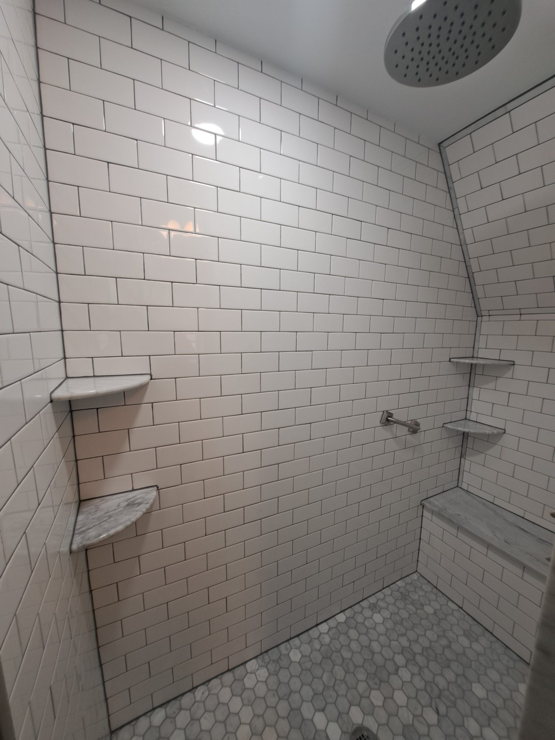 Tiled shower with white brick-like walls, stone floor, built-in seat, and corner shelves.