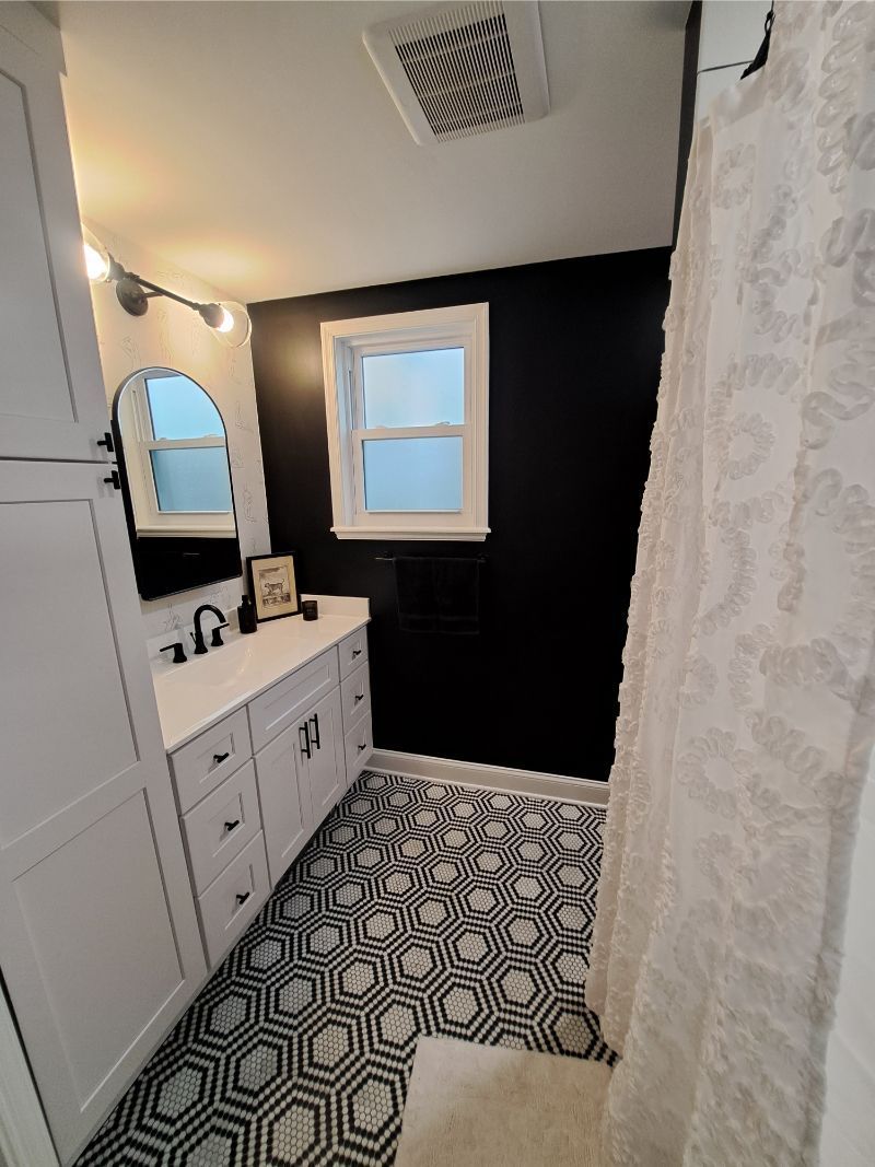 Bathroom with black accent wall, white vanity, patterned tile floor, and a window.