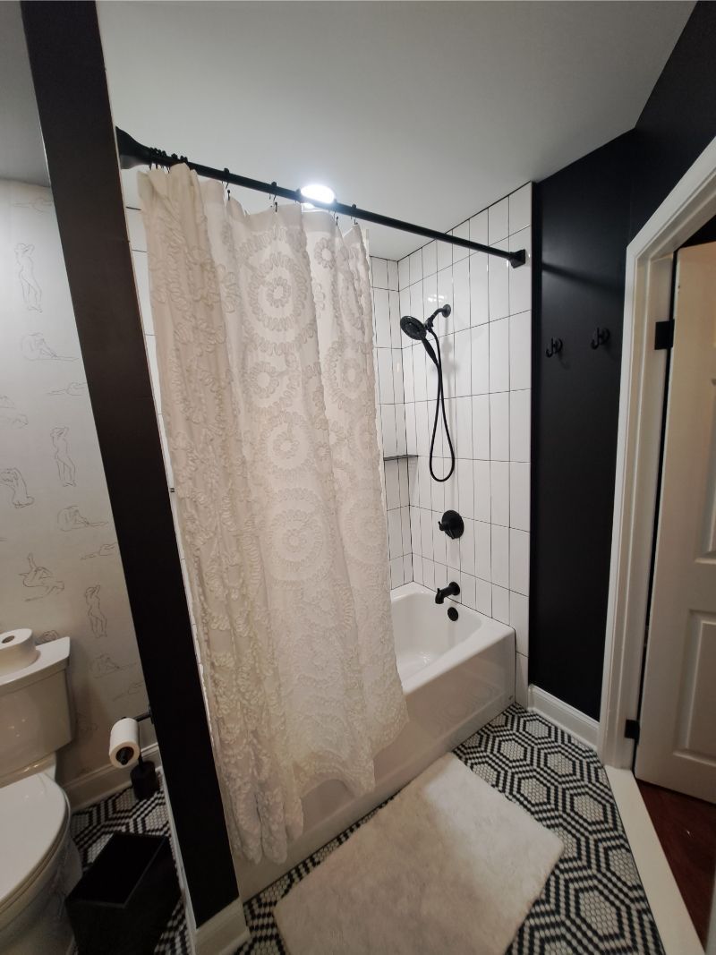 Bathroom with white subway tile shower, black fixtures, and patterned floor.