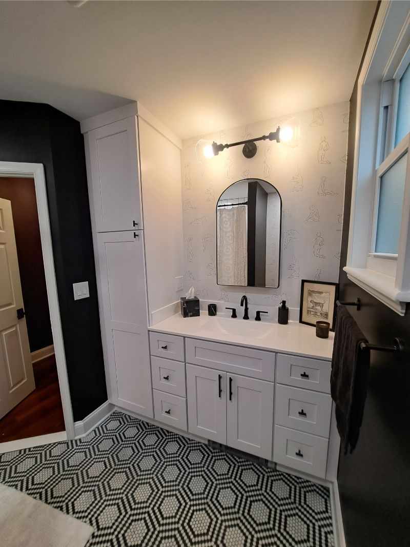 Bathroom with black and white hexagon floor tiles, white cabinets, and black fixtures.