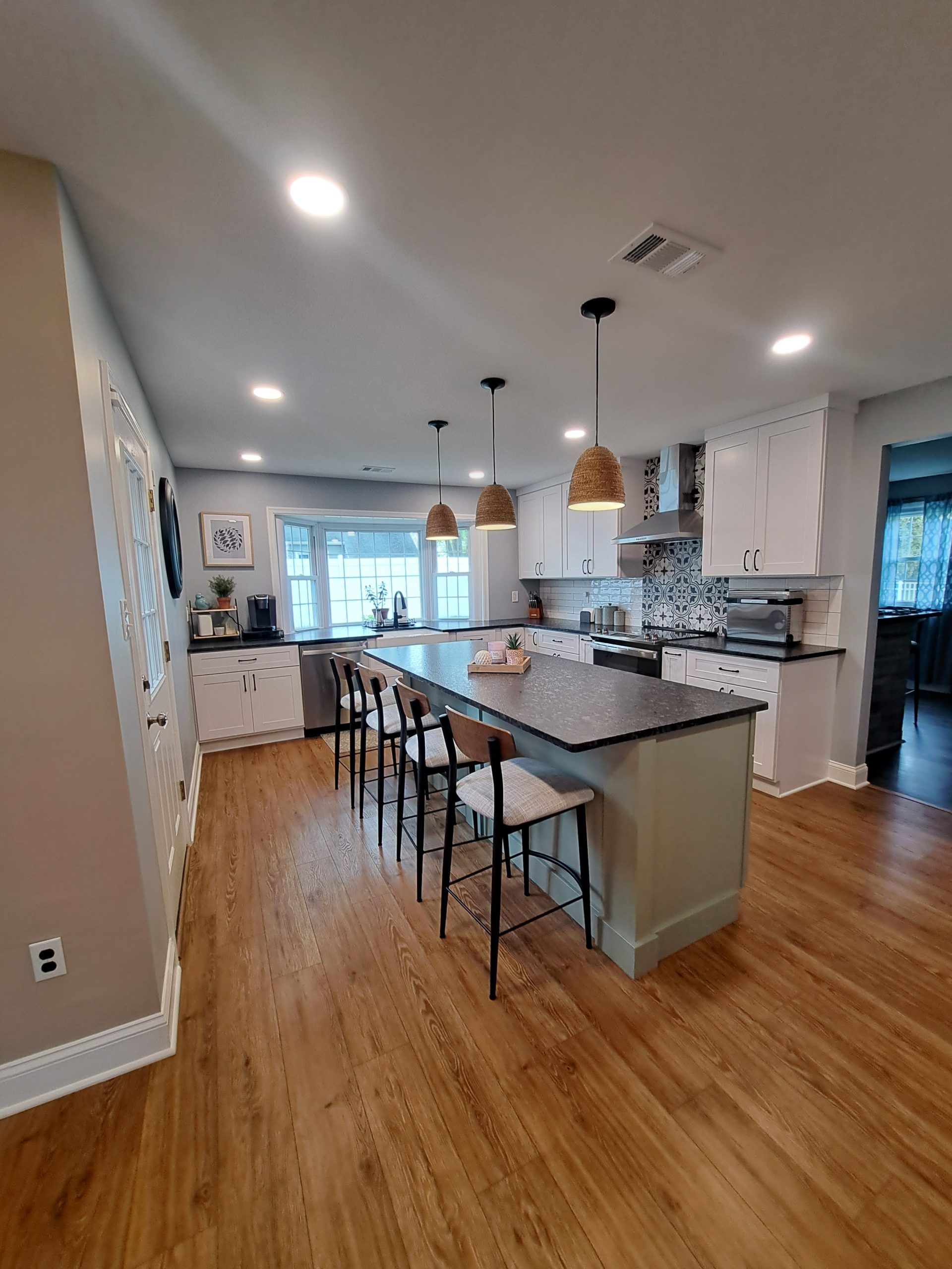 Kitchen with island and bar stools, white cabinets, hardwood floors, and overhead lighting.