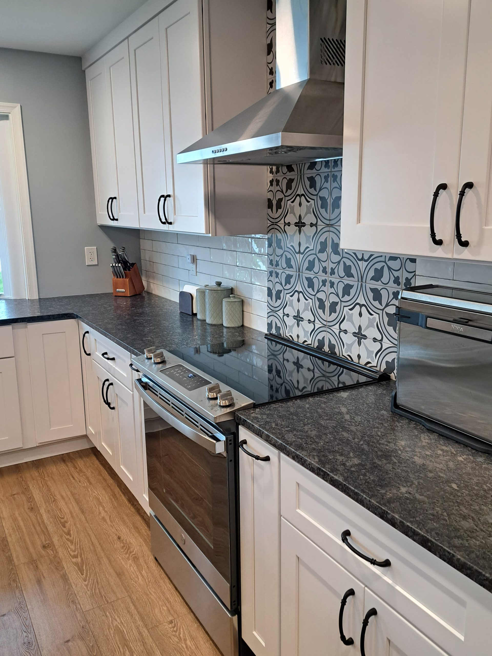 White kitchen cabinets, black countertops, stainless steel appliances, and patterned backsplash.
