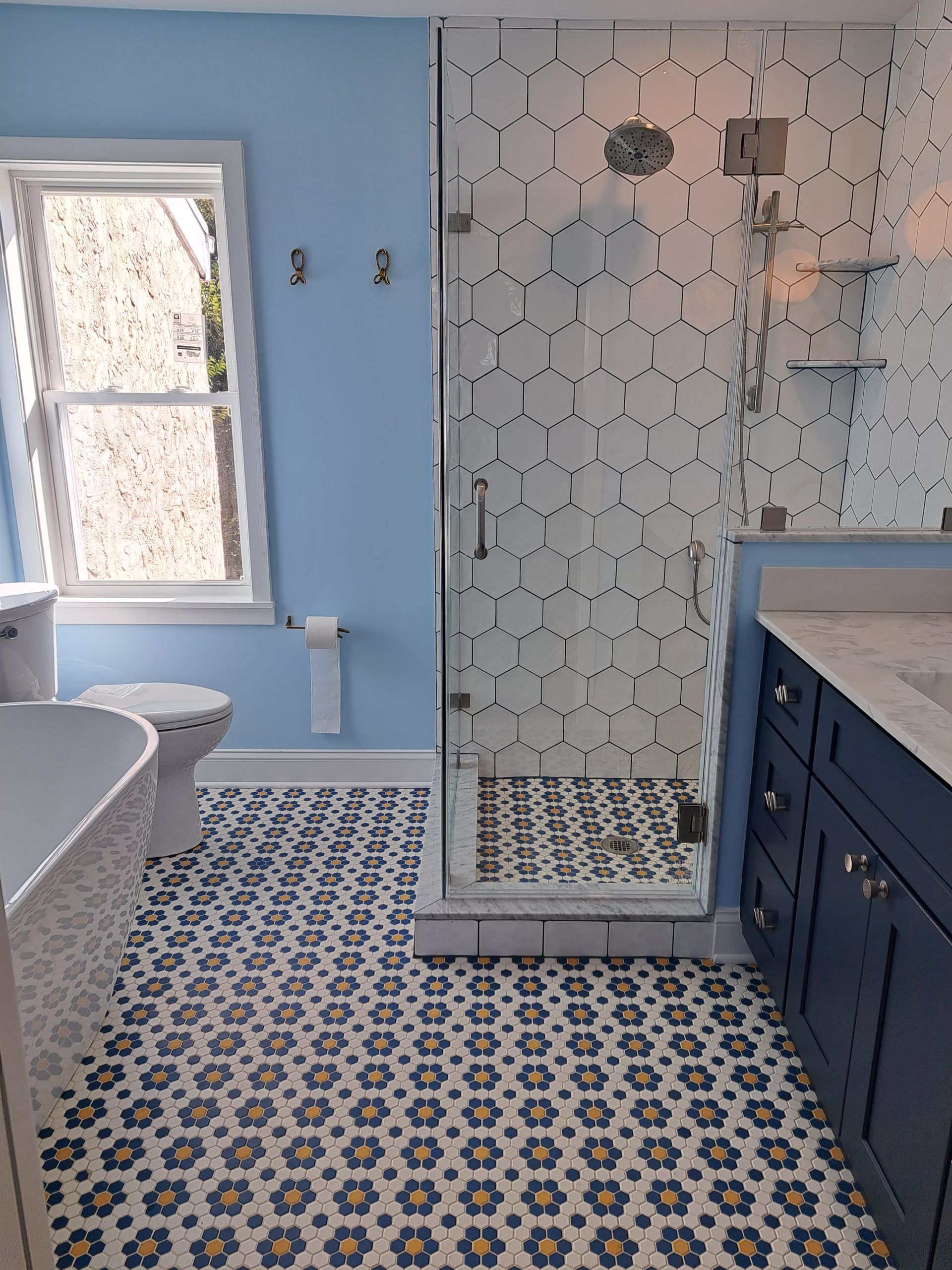 Bathroom with blue walls, patterned floor tiles, glass shower, and navy vanity.
