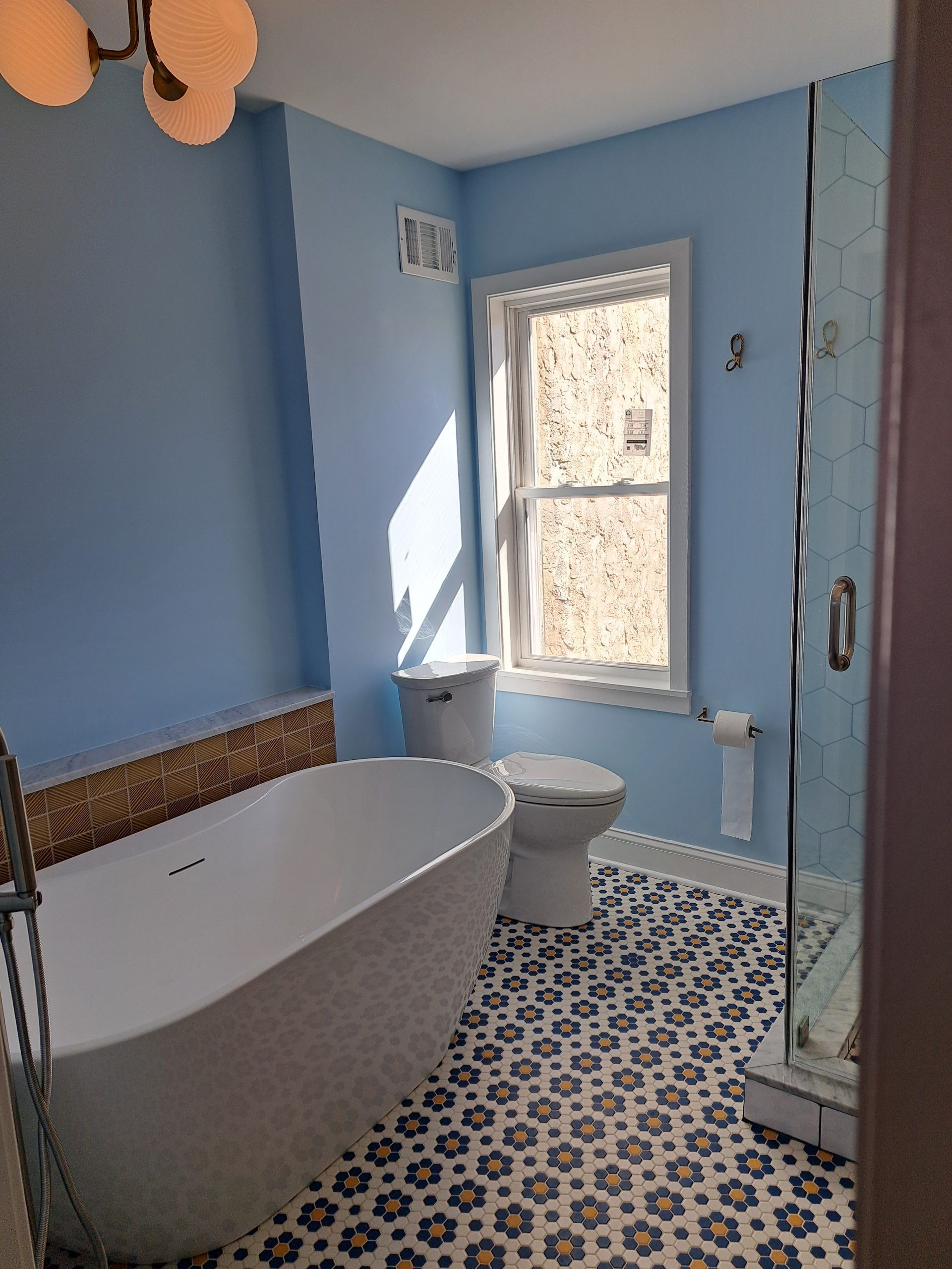 Bathroom with blue walls, patterned floor, white tub and toilet, window.