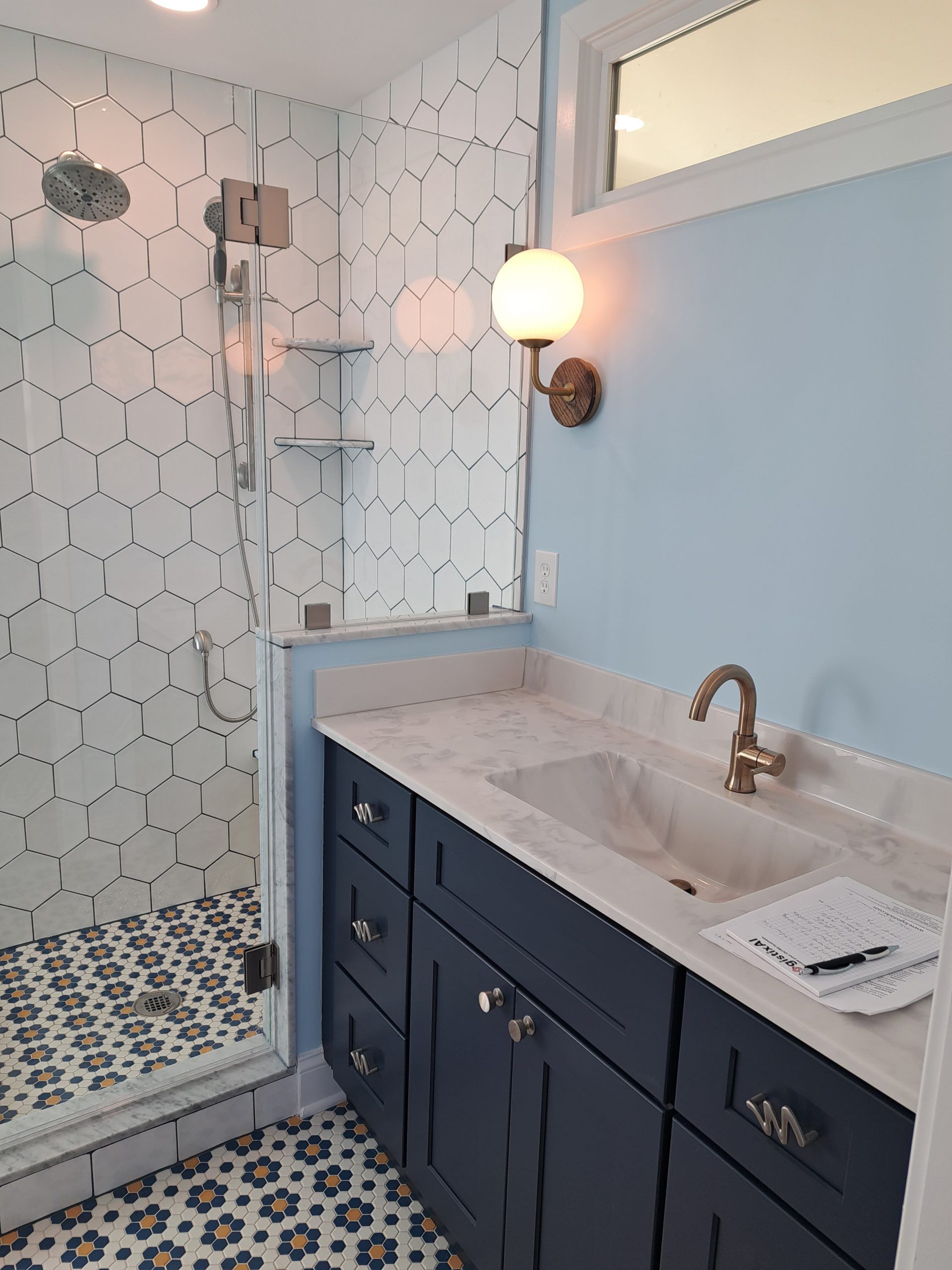 Bathroom with blue vanity, patterned tile shower, marble countertop, and gold fixtures.