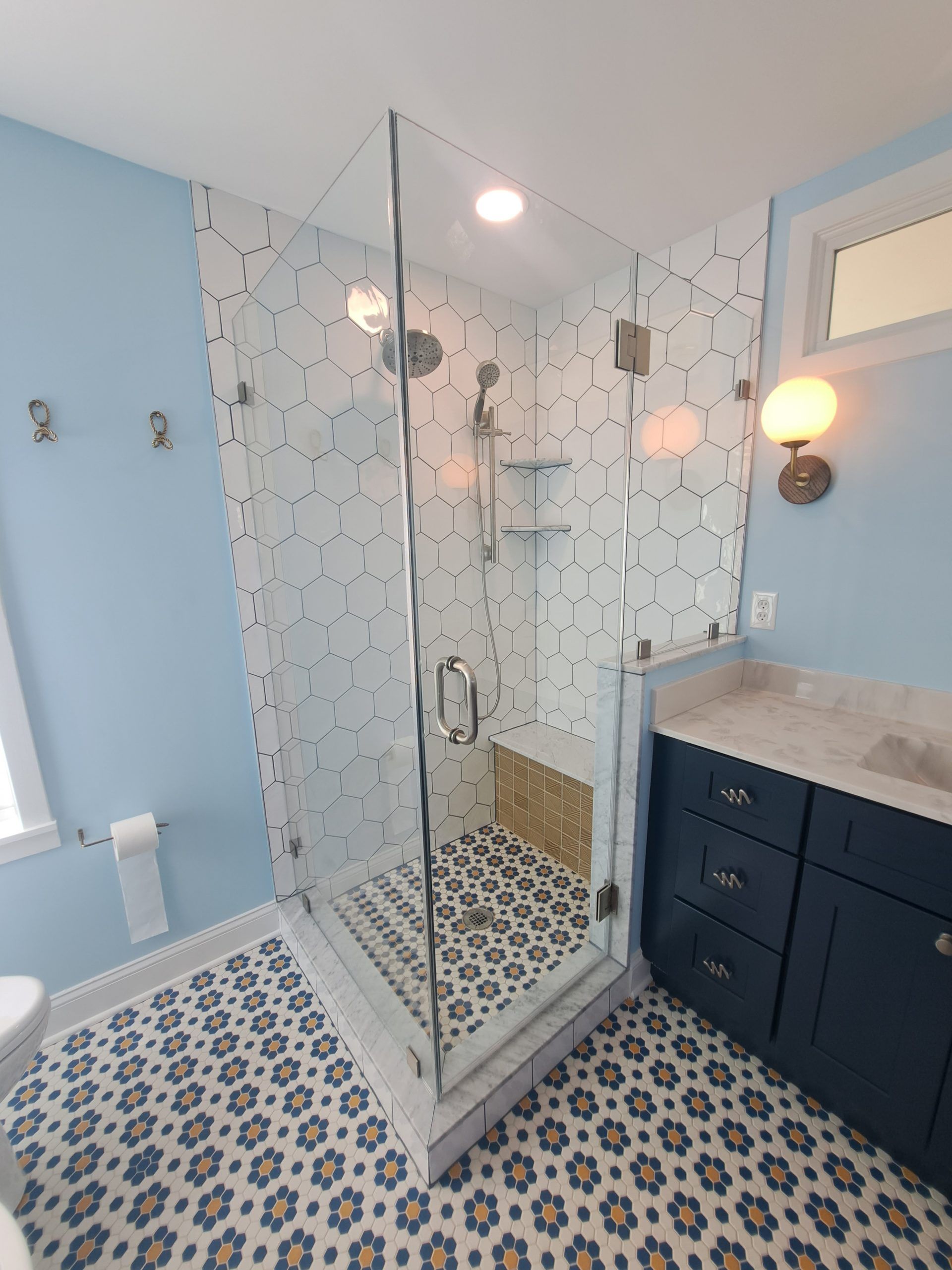 Modern bathroom with glass shower, patterned tile, blue walls, and dark blue vanity.
