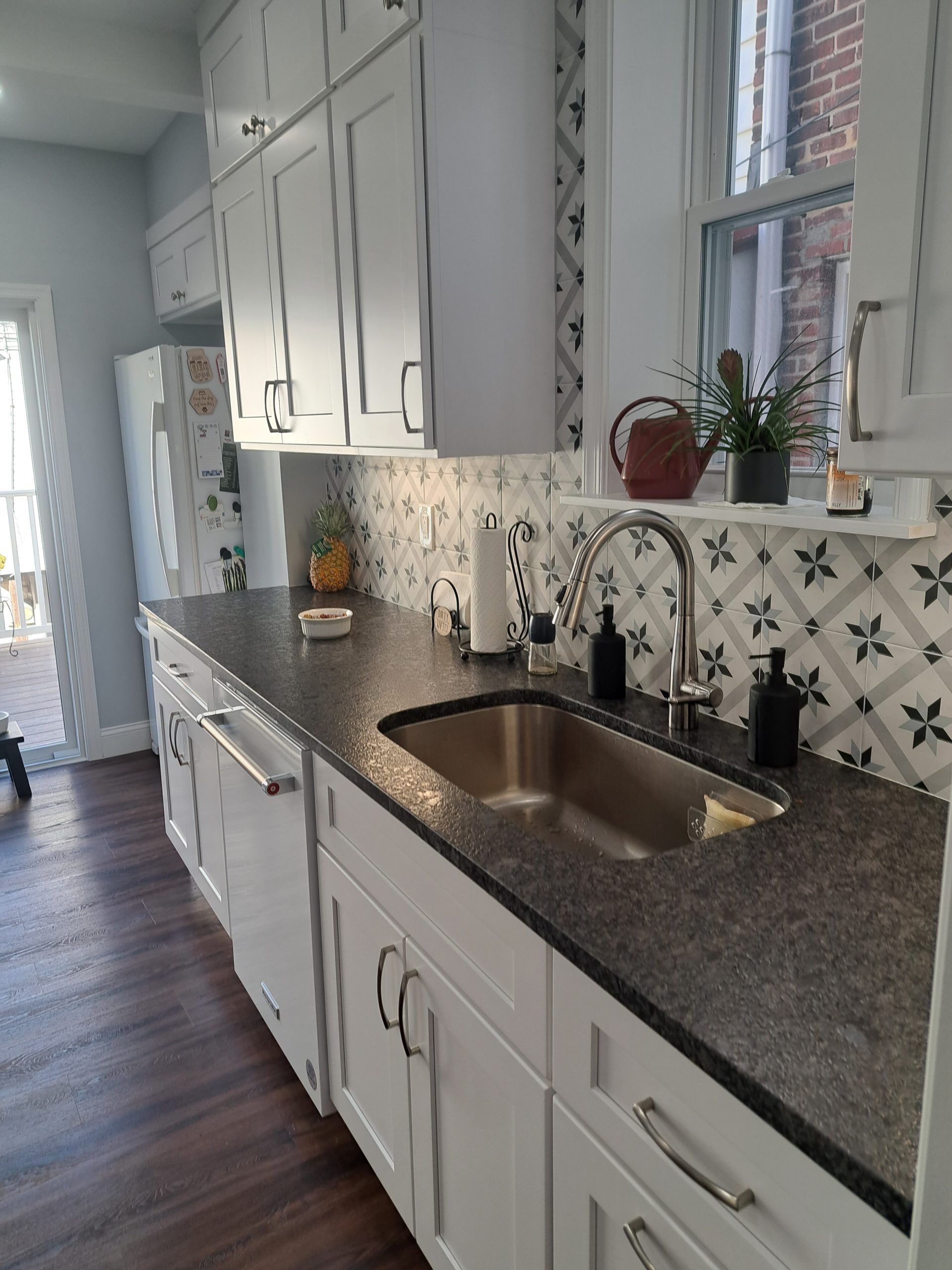 White kitchen with dark countertops, stainless steel sink, and patterned backsplash.