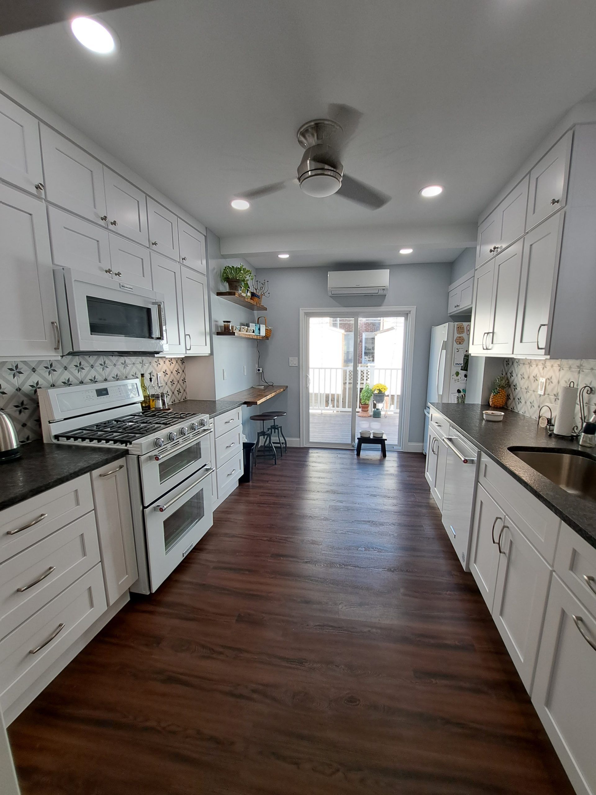 White kitchen with dark countertops and wood flooring, leading to a door.