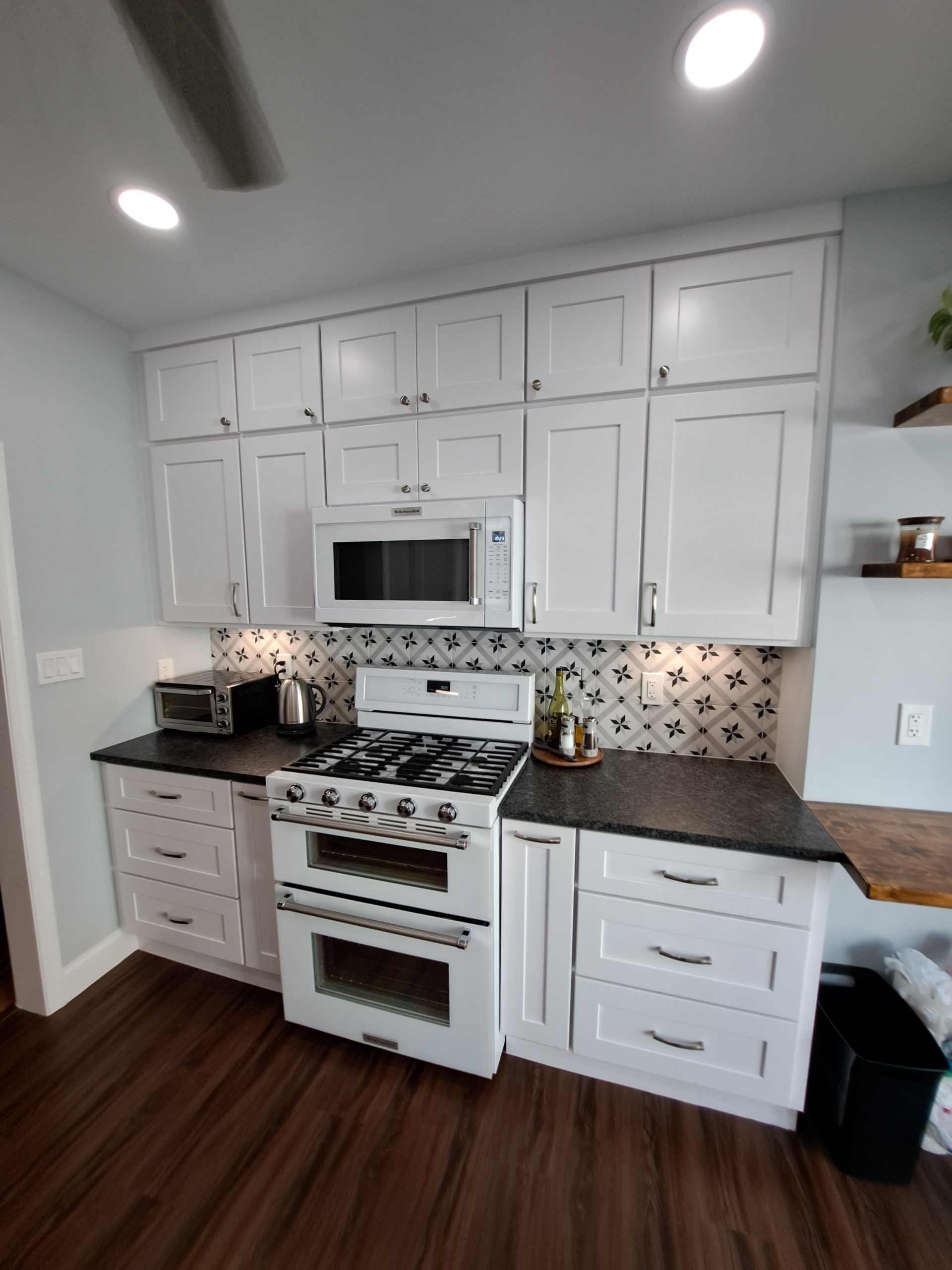 White kitchen with stove, cabinets, and black countertops; blue walls and wood floors.