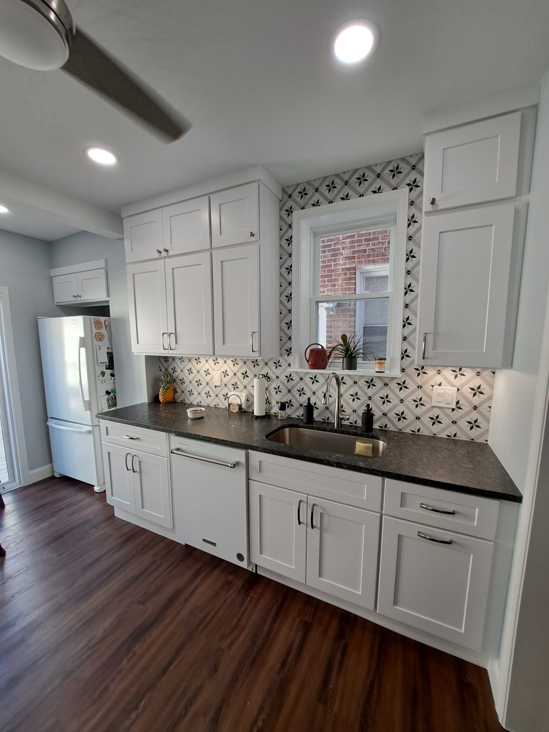 White kitchen with dark countertops, wood floor, and decorative backsplash.