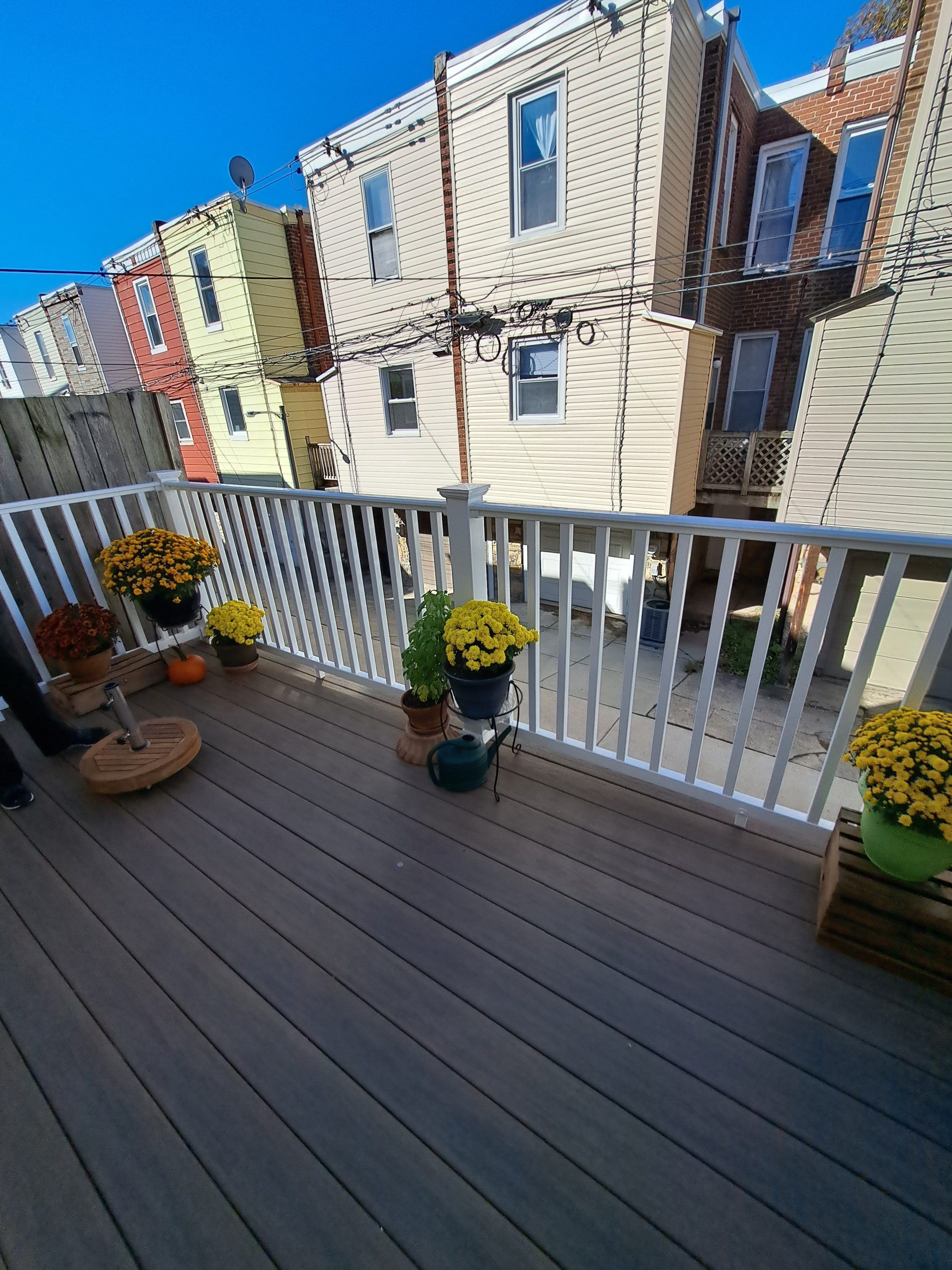 Wooden deck with white railing, potted mums, and view of neighboring buildings.