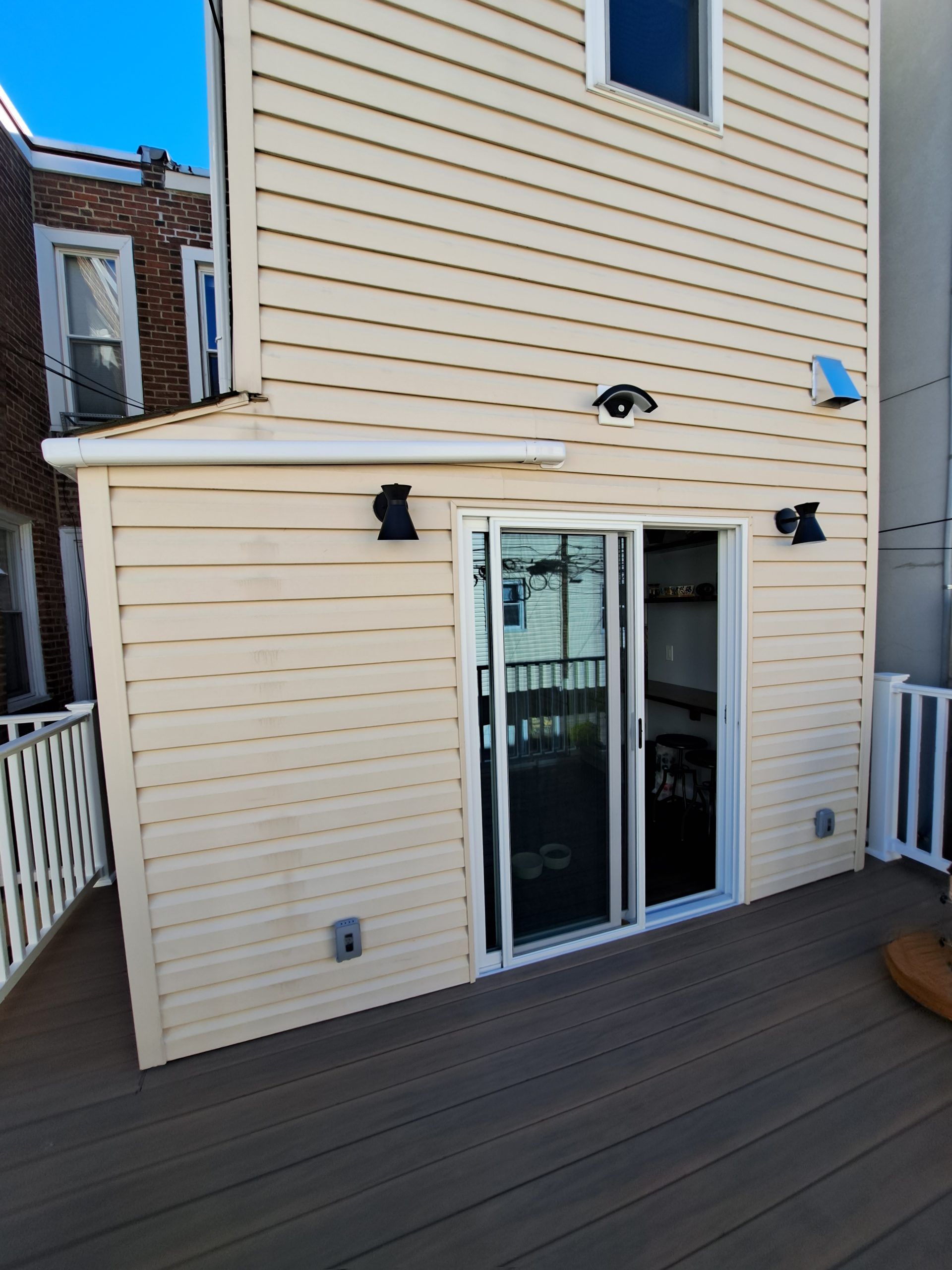 Back exterior of a two-story building with sliding glass doors, tan siding, and a wooden deck.
