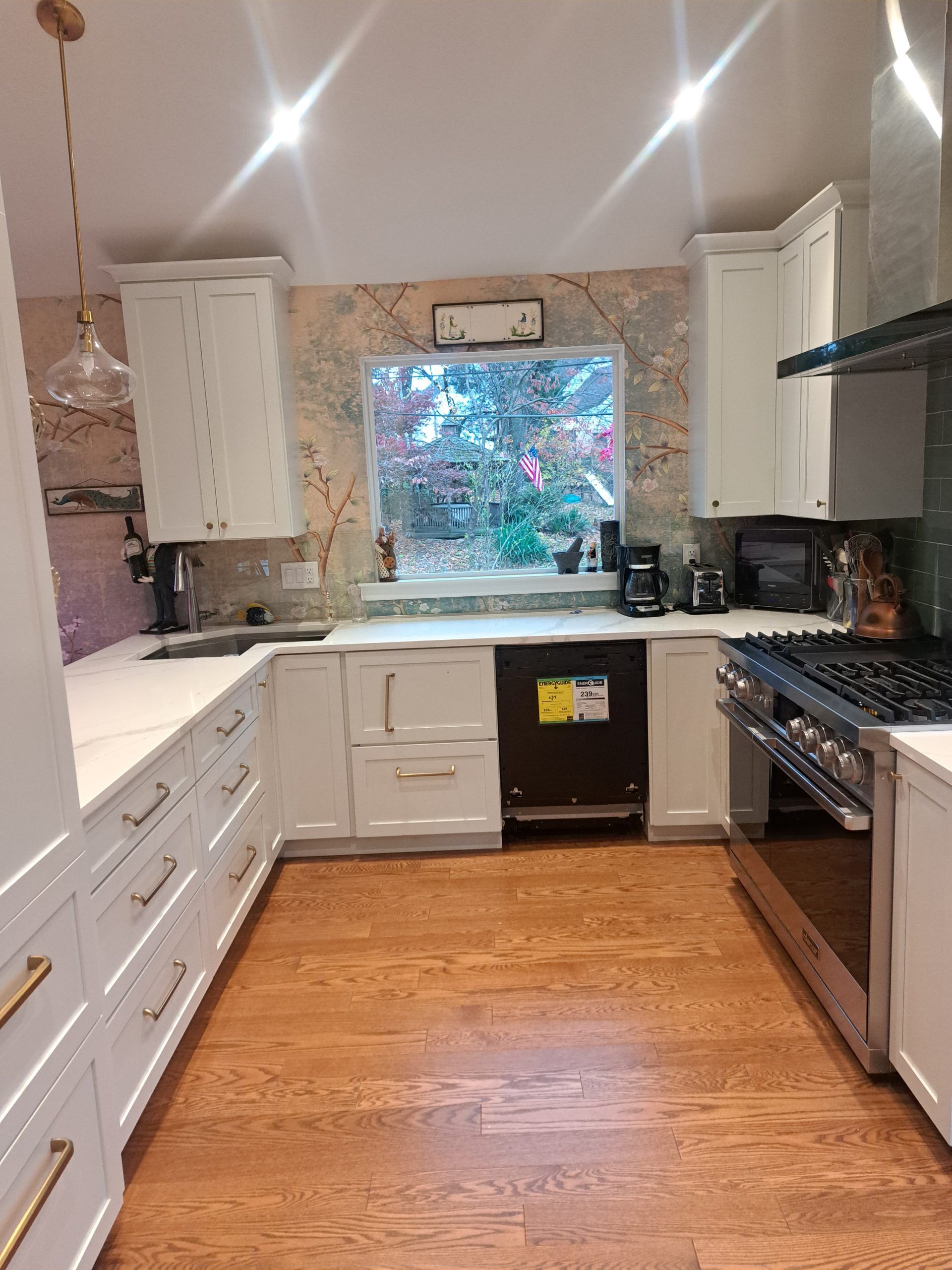 White kitchen with light wood floors, cabinets, and appliances; window in the center.