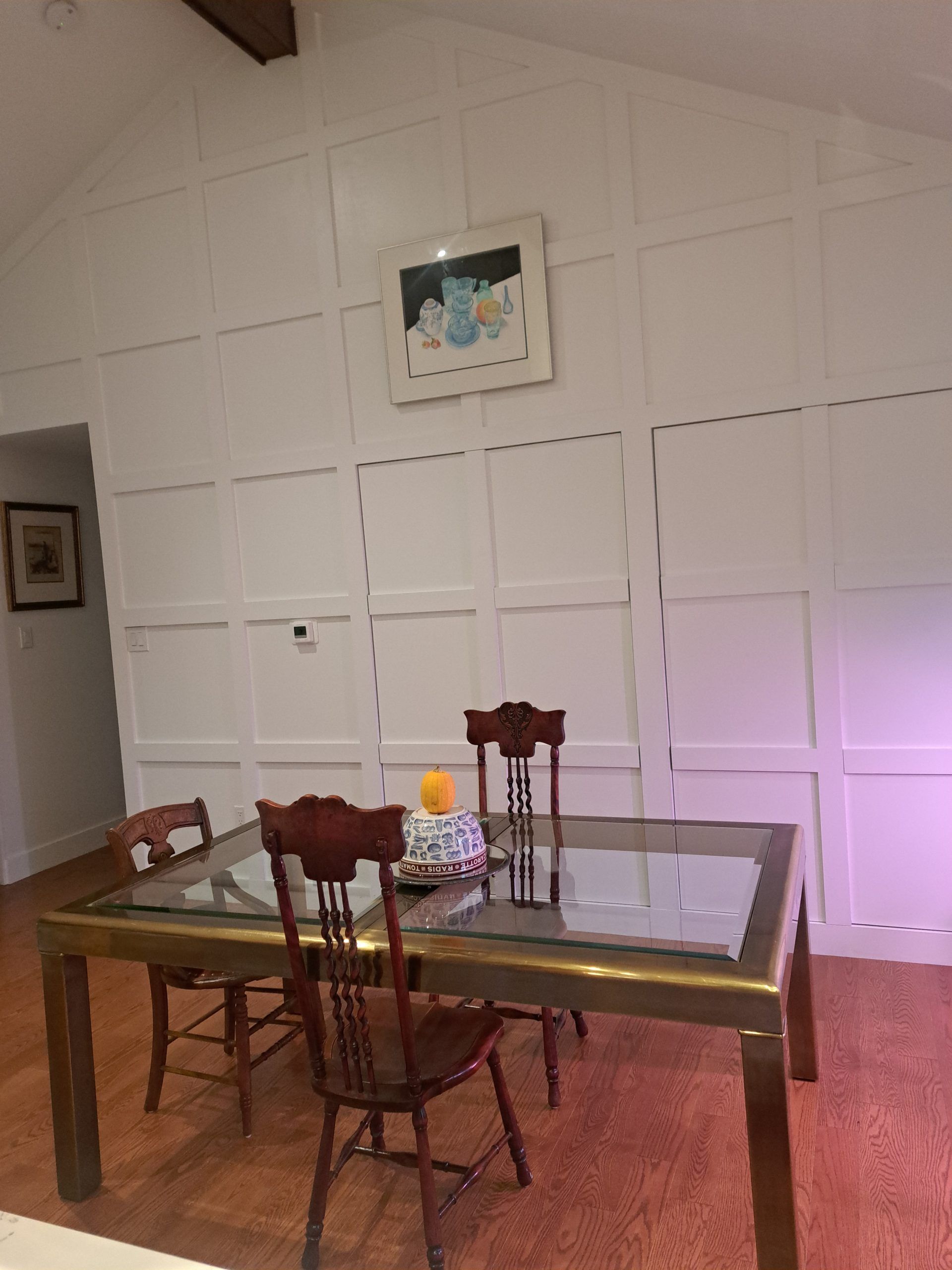 Dining room with paneled white walls, a wooden table and chairs, and a framed picture.
