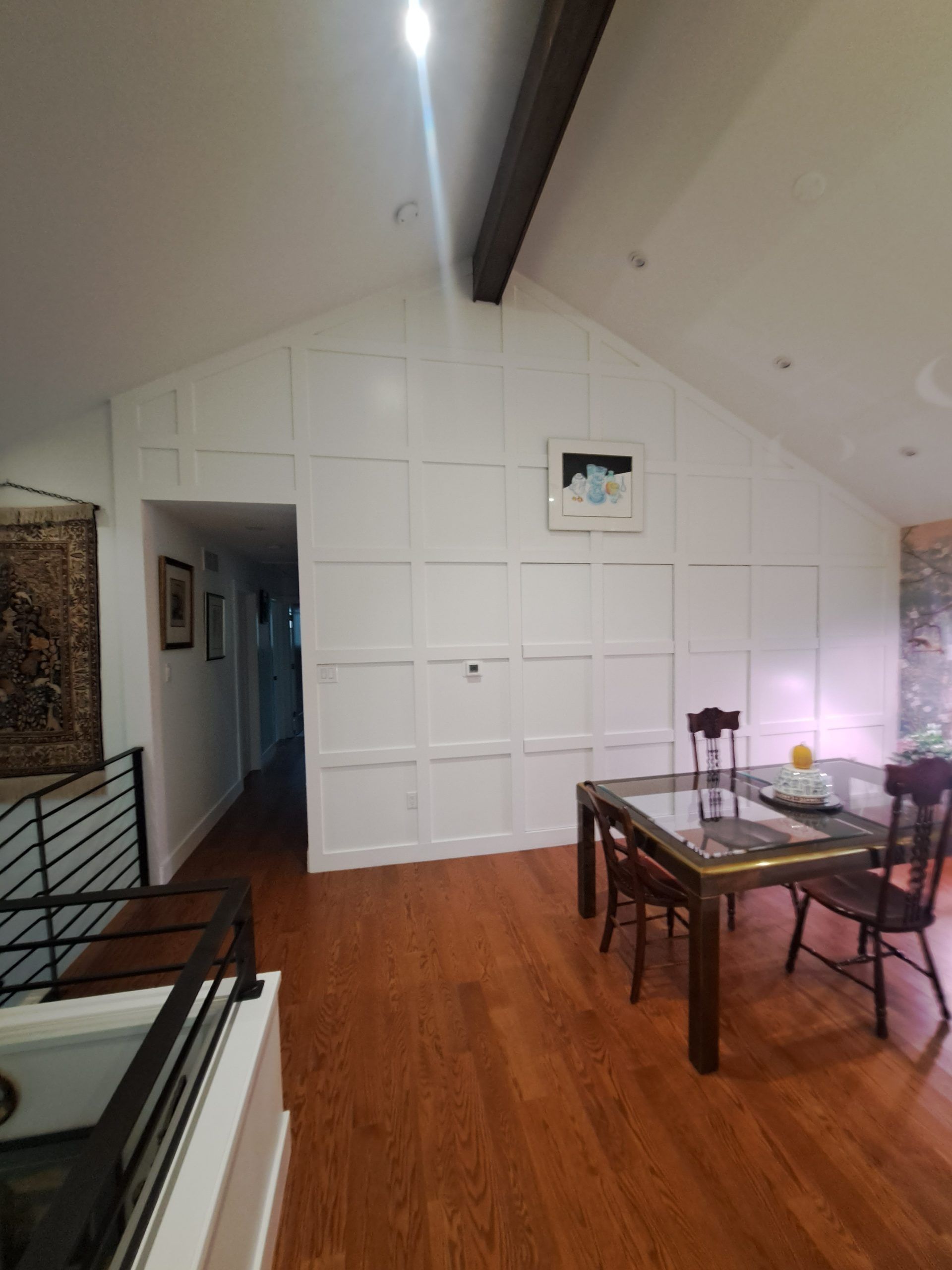 Dining room with wood floor and white panel wall. Table and chairs in front. Hallway to the left.
