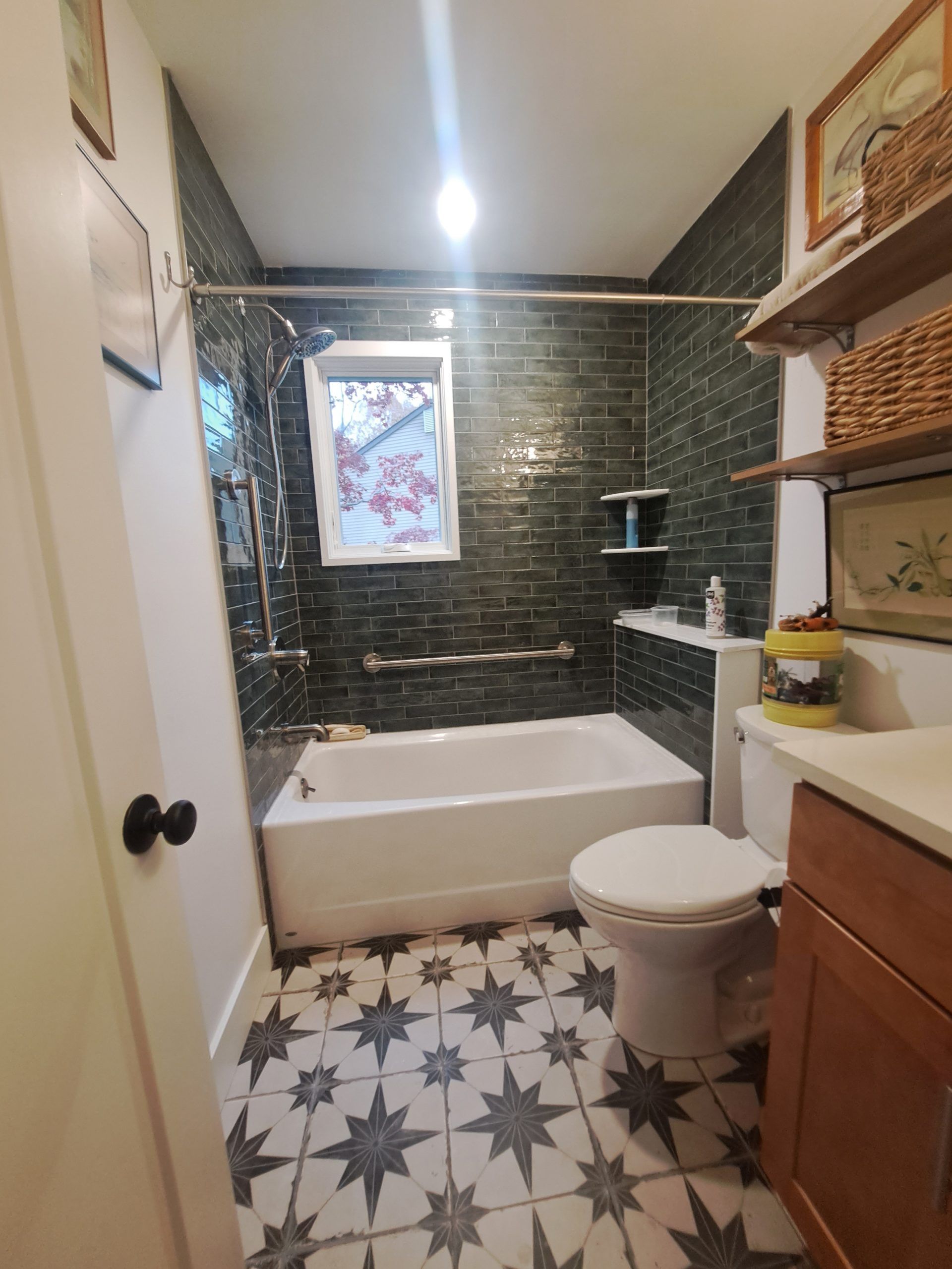 Bathroom with dark tiled shower, white tub, patterned floor, and wooden vanity.