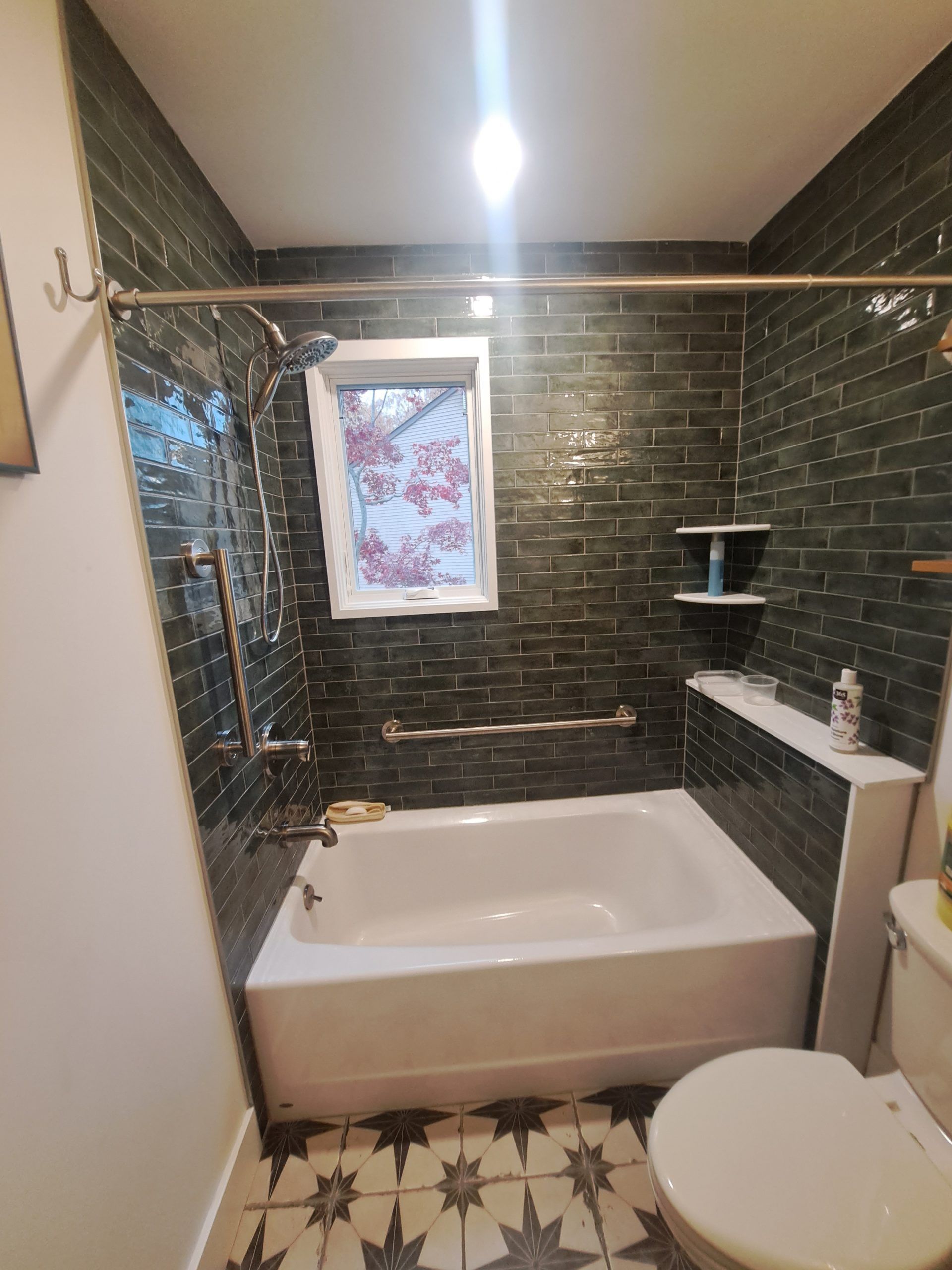 Dark tiled bathroom with tub, toilet, and window. Metallic fixtures, white tub, and patterned floor.