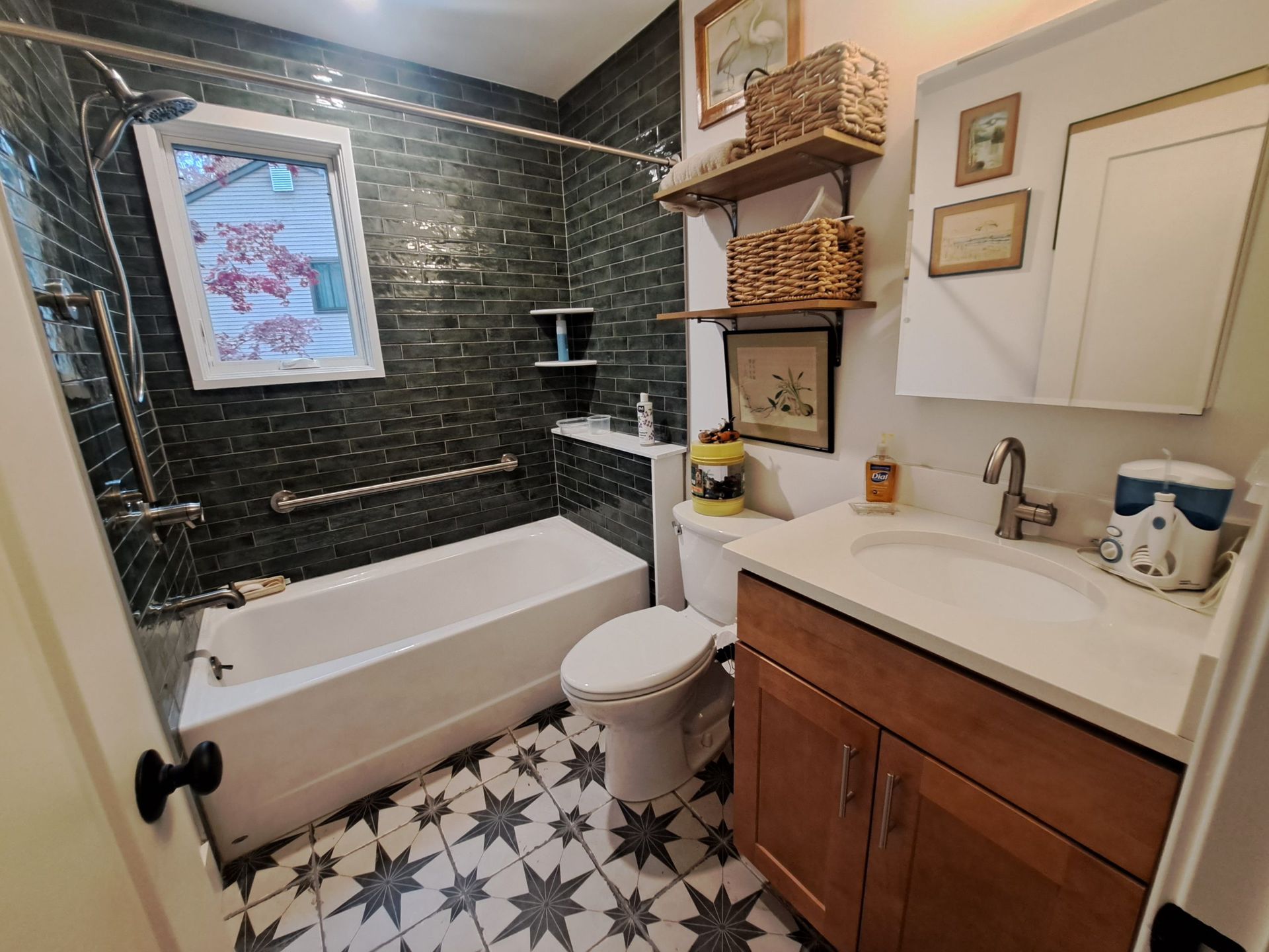 Small bathroom with dark green tiled walls, white bathtub, vanity, and star pattern floor.