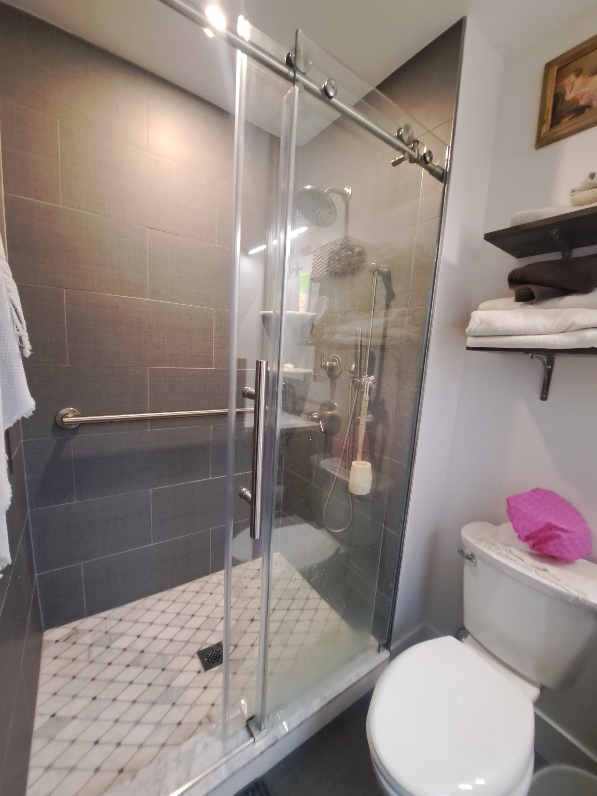 Bathroom with a glass-enclosed shower, toilet, towel rack, and dark gray tile.