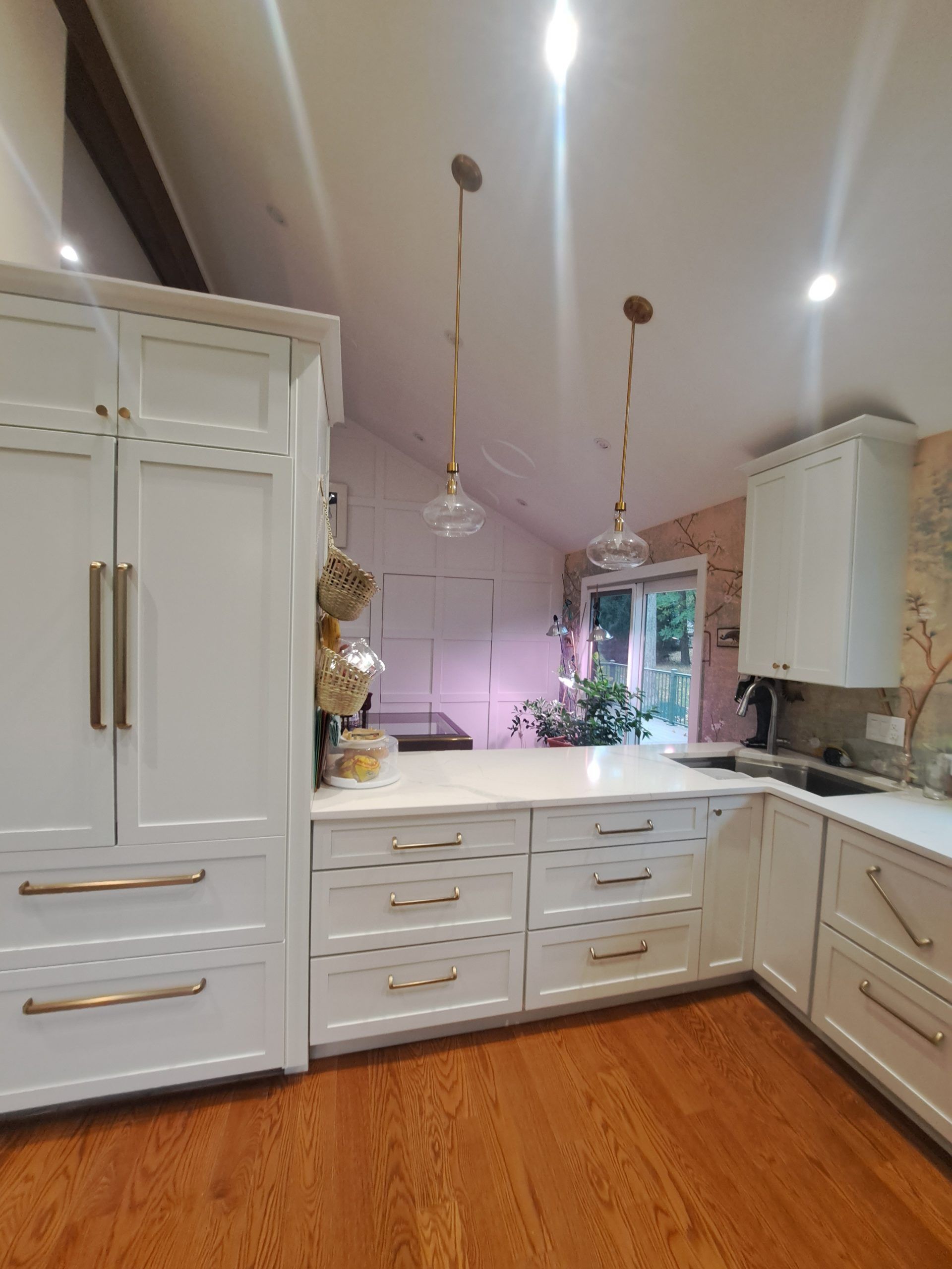 White kitchen with golden hardware, wood floors, and pendant lights.