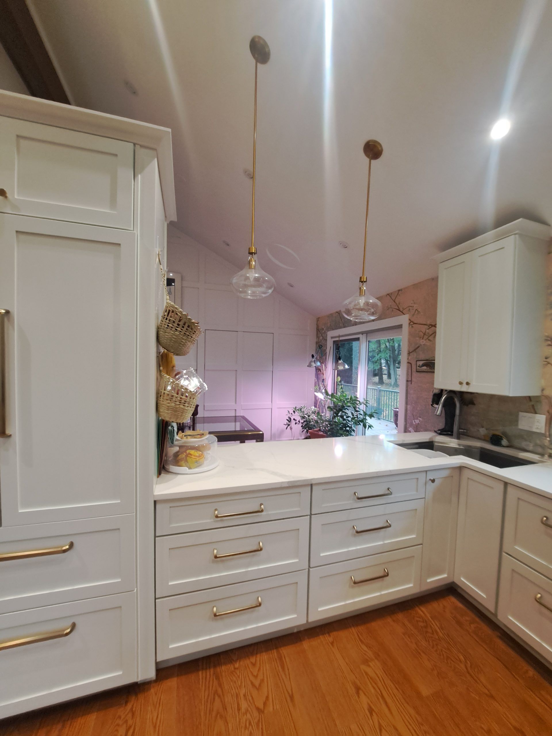 White kitchen with gold hardware, two pendant lights, and a view of a garden.