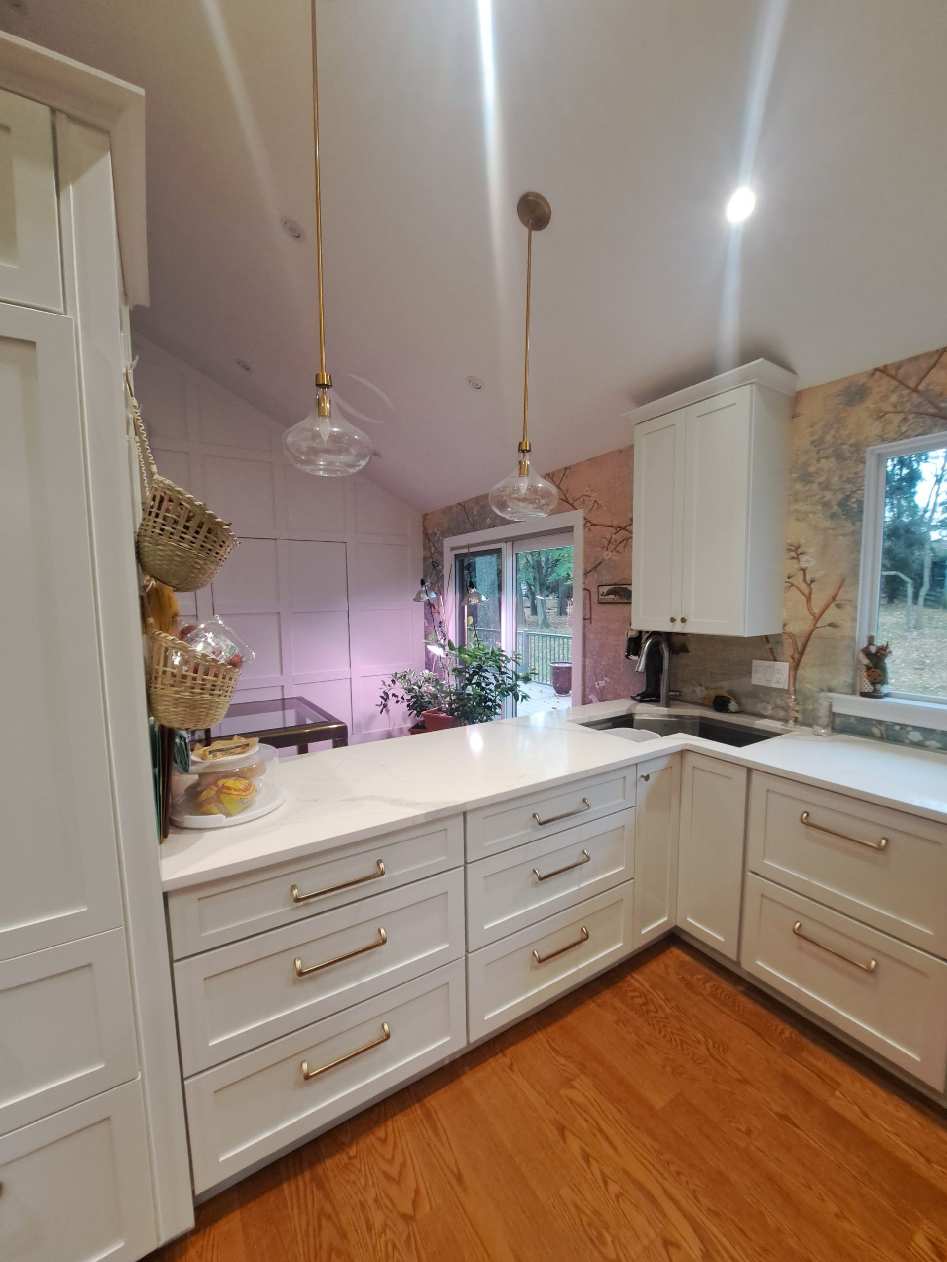 White kitchen with a countertop, cabinets, and two hanging lights. Wooden floor and a window.