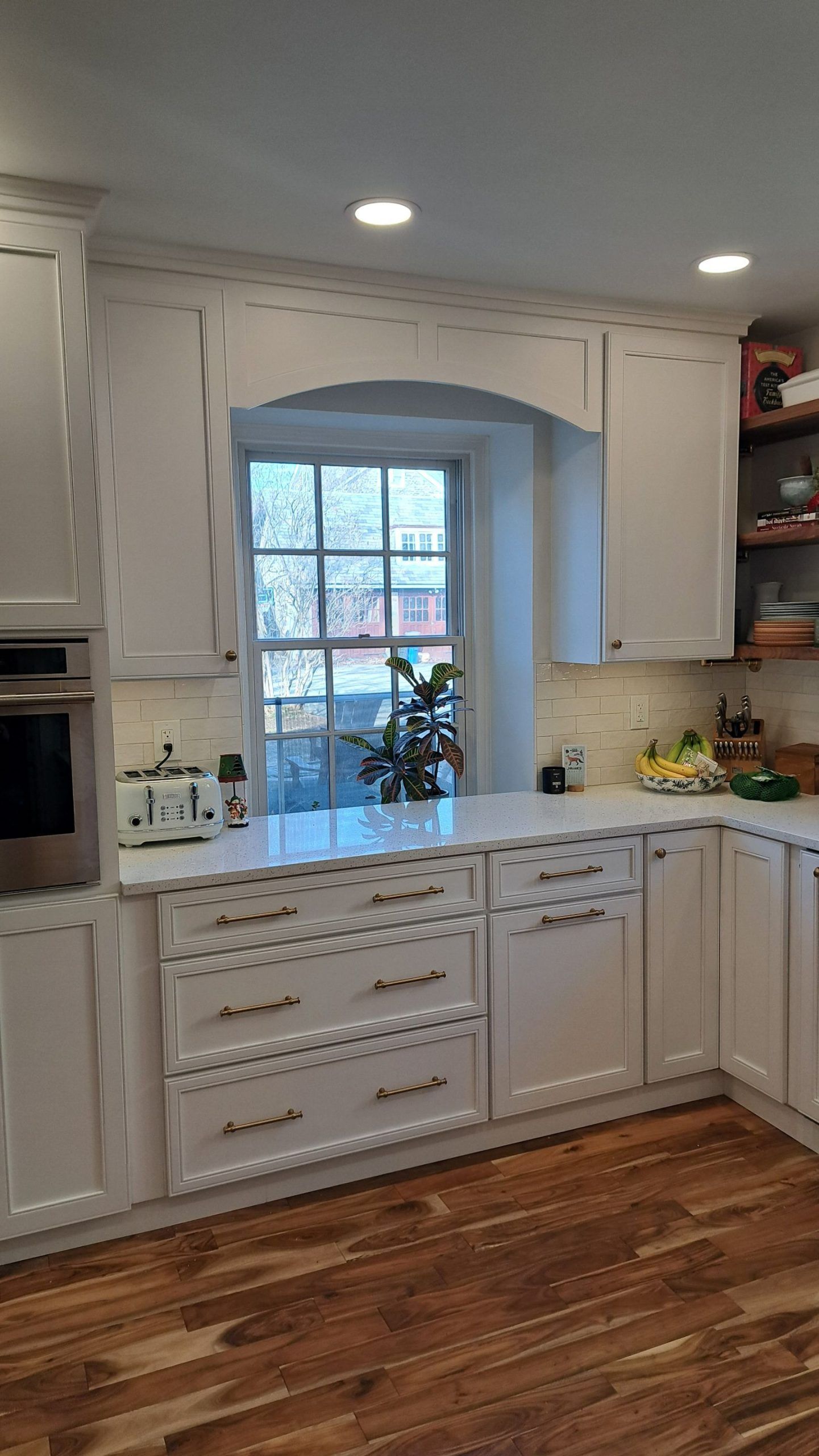White kitchen with cabinets, window, and wooden floors.