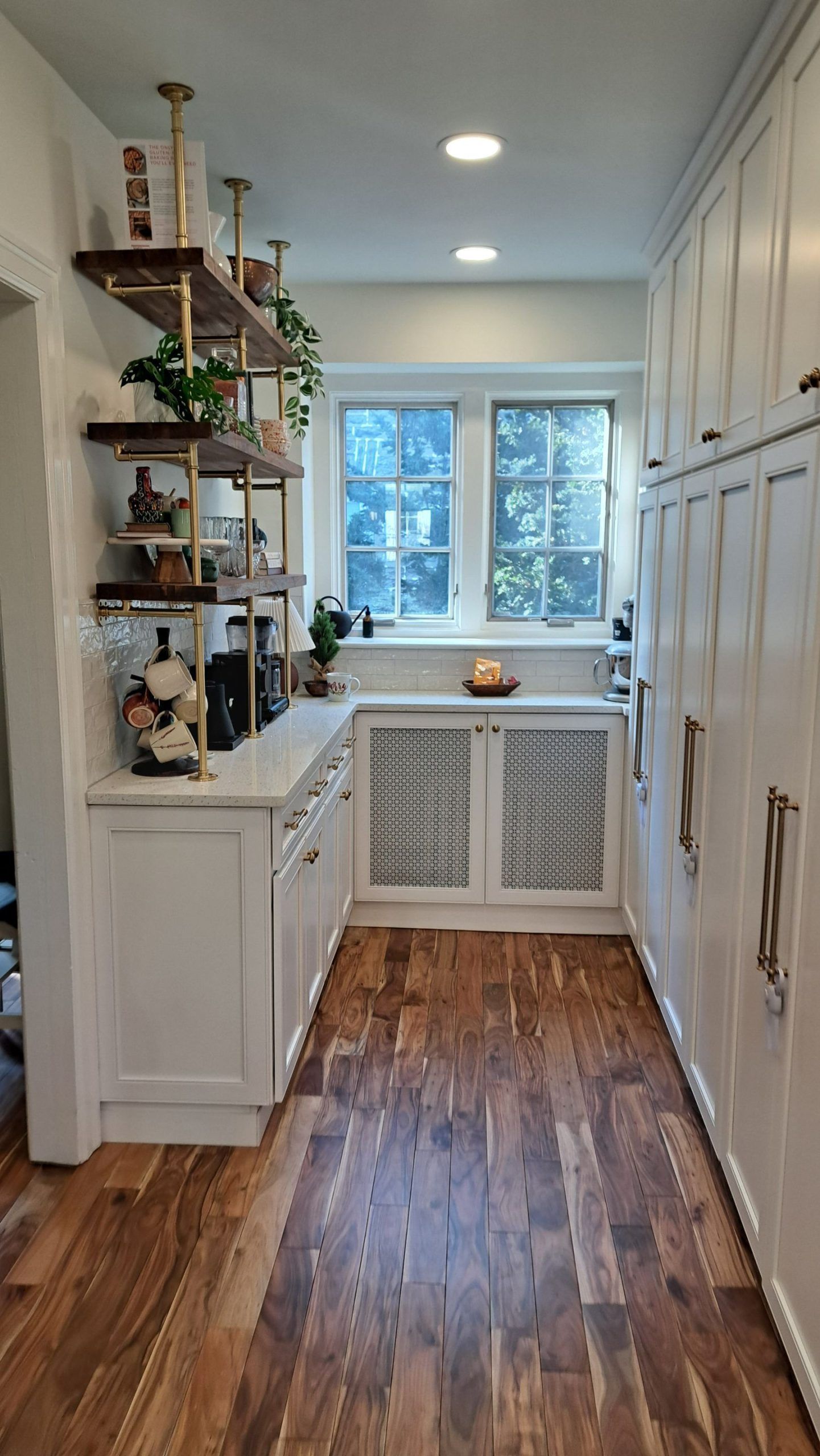 White kitchen with wooden floors, shelving, cabinets, and a window.