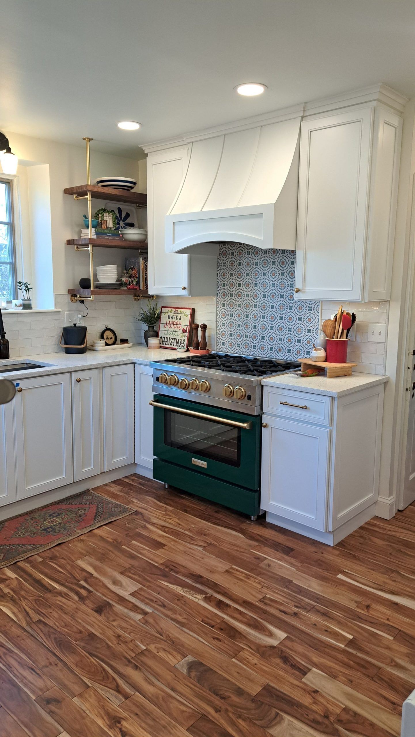 Green stove in white kitchen with wooden floors and open shelving.