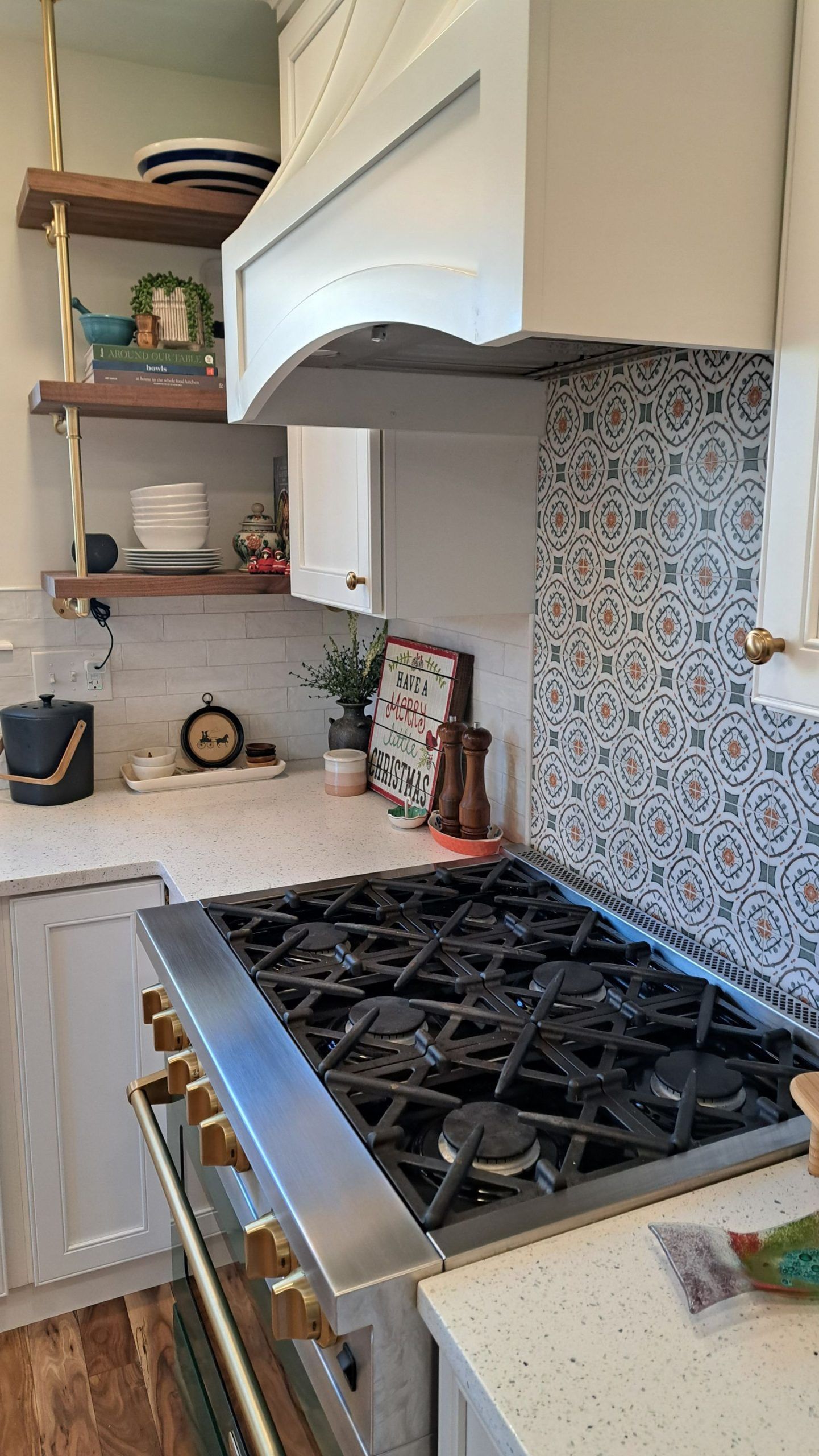 Kitchen with stove, range hood, tiled backsplash, and open shelving with dishes.