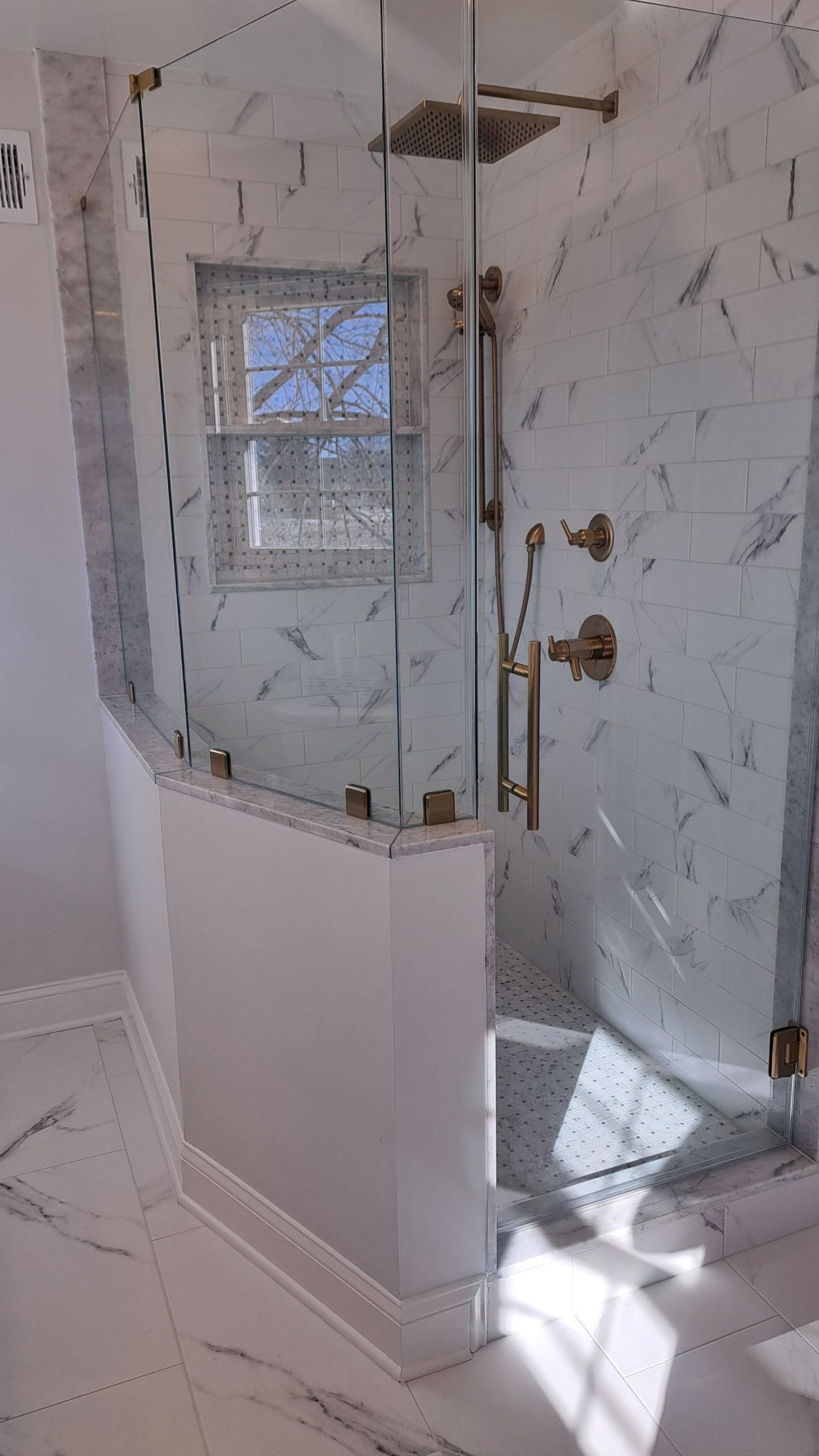 Shower with marble walls, glass door, and brass fixtures.