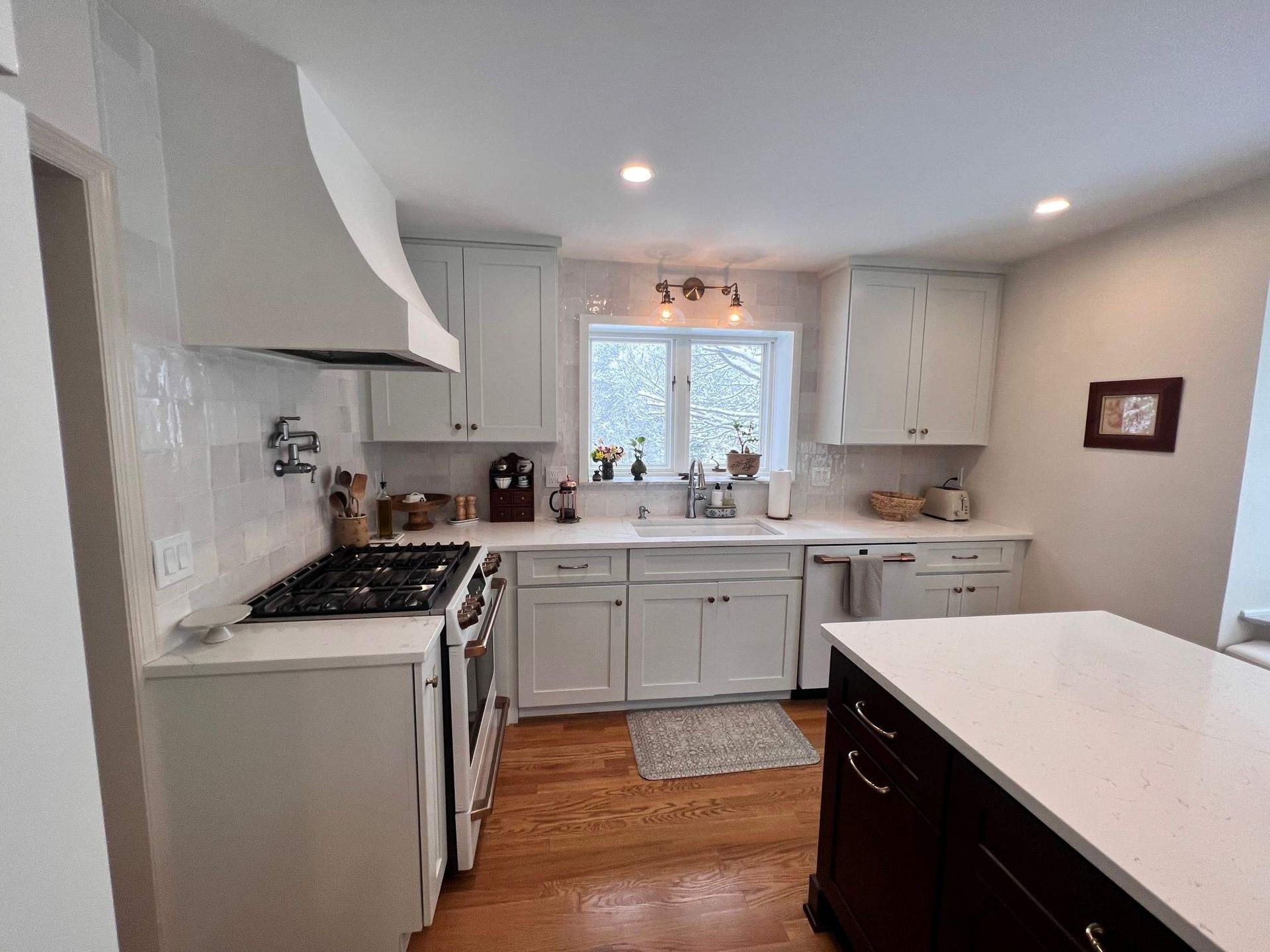 White kitchen with stove, cabinets, and island; hardwood floor.