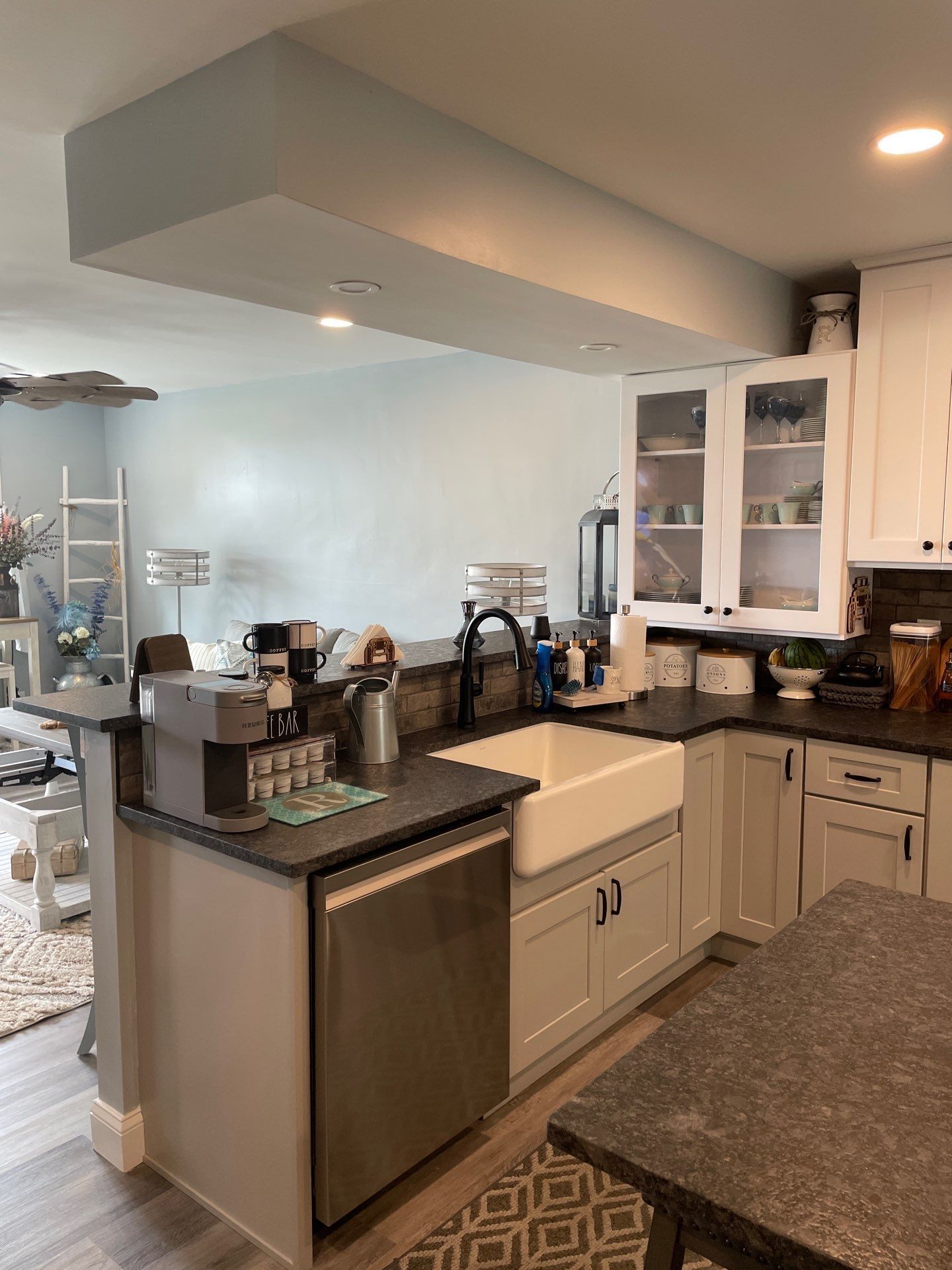 Kitchen with white cabinets, farmhouse sink, black countertops, and a coffee machine.