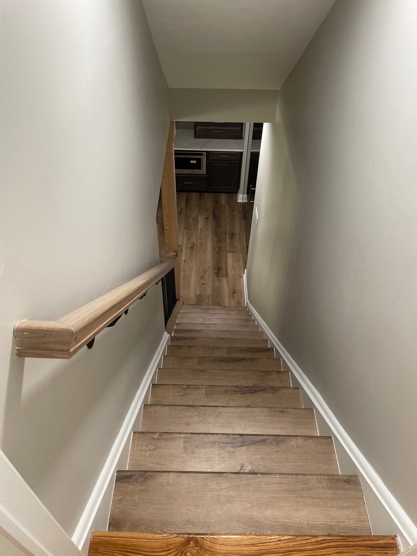 Staircase descending into a lower level with wood-look flooring and a light-colored handrail on the left.
