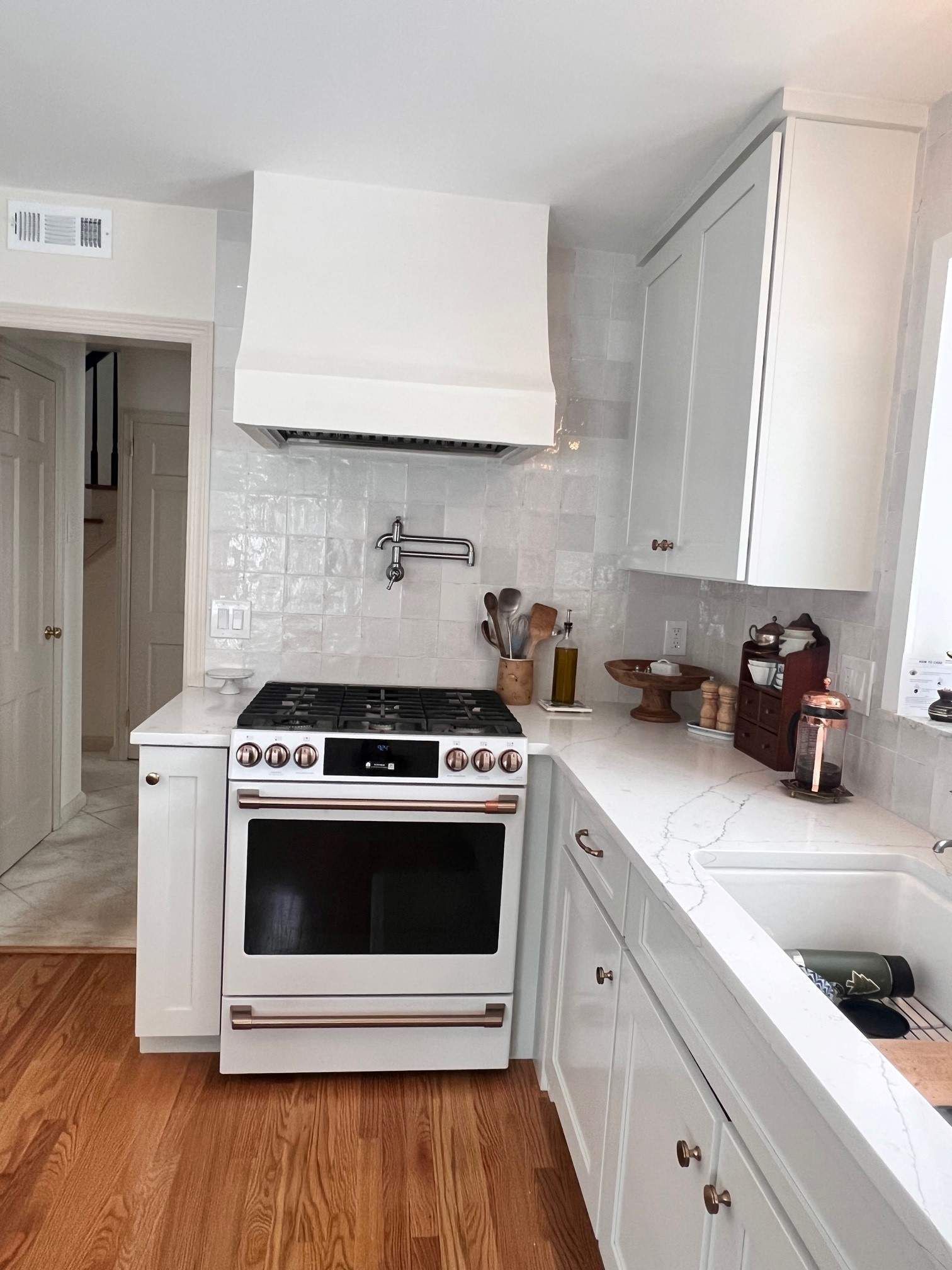 White kitchen with stove, range hood, cabinets, and wood flooring.
