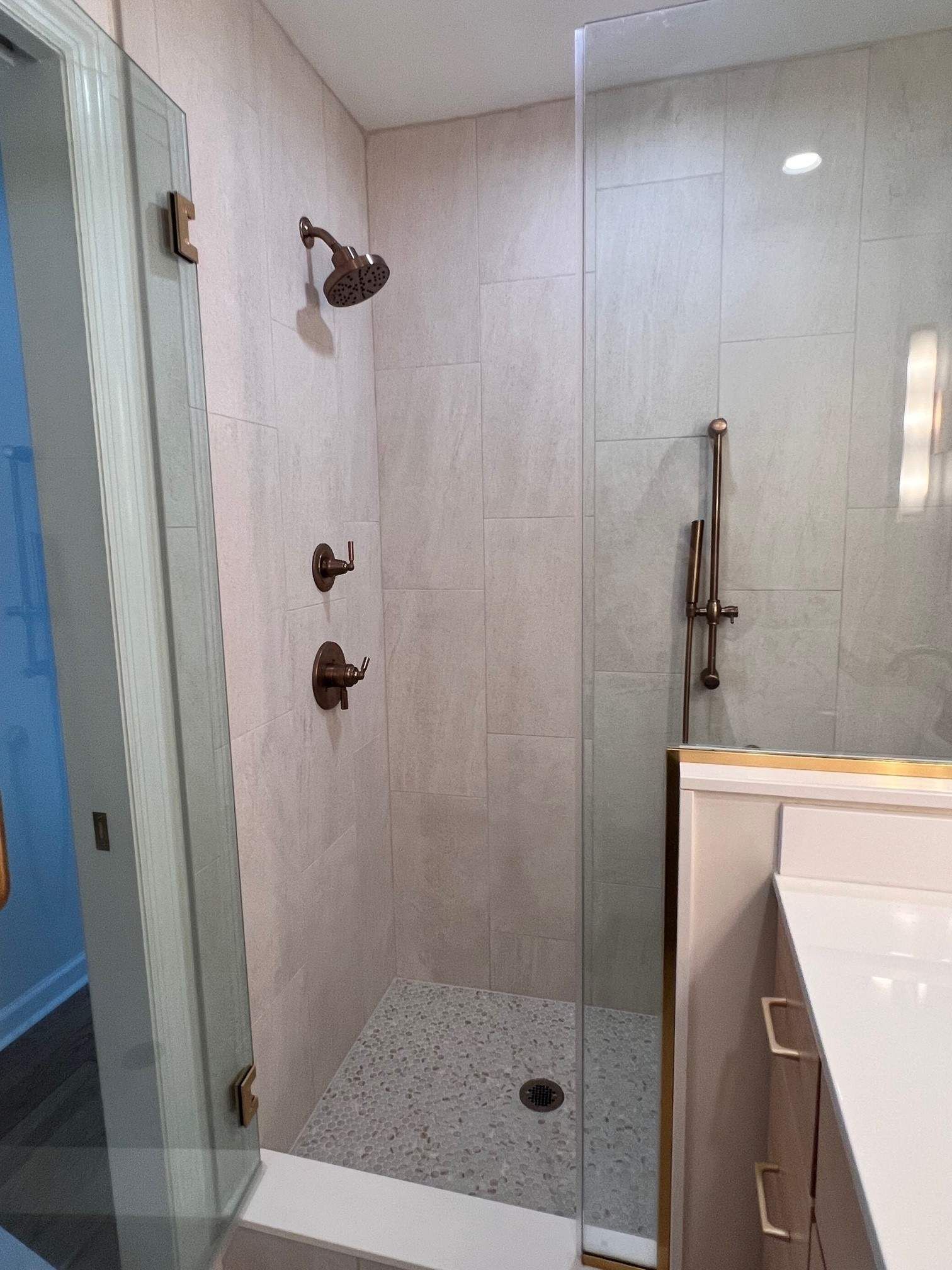 Modern bathroom with a glass-enclosed shower, featuring stone tile floor and bronze fixtures.