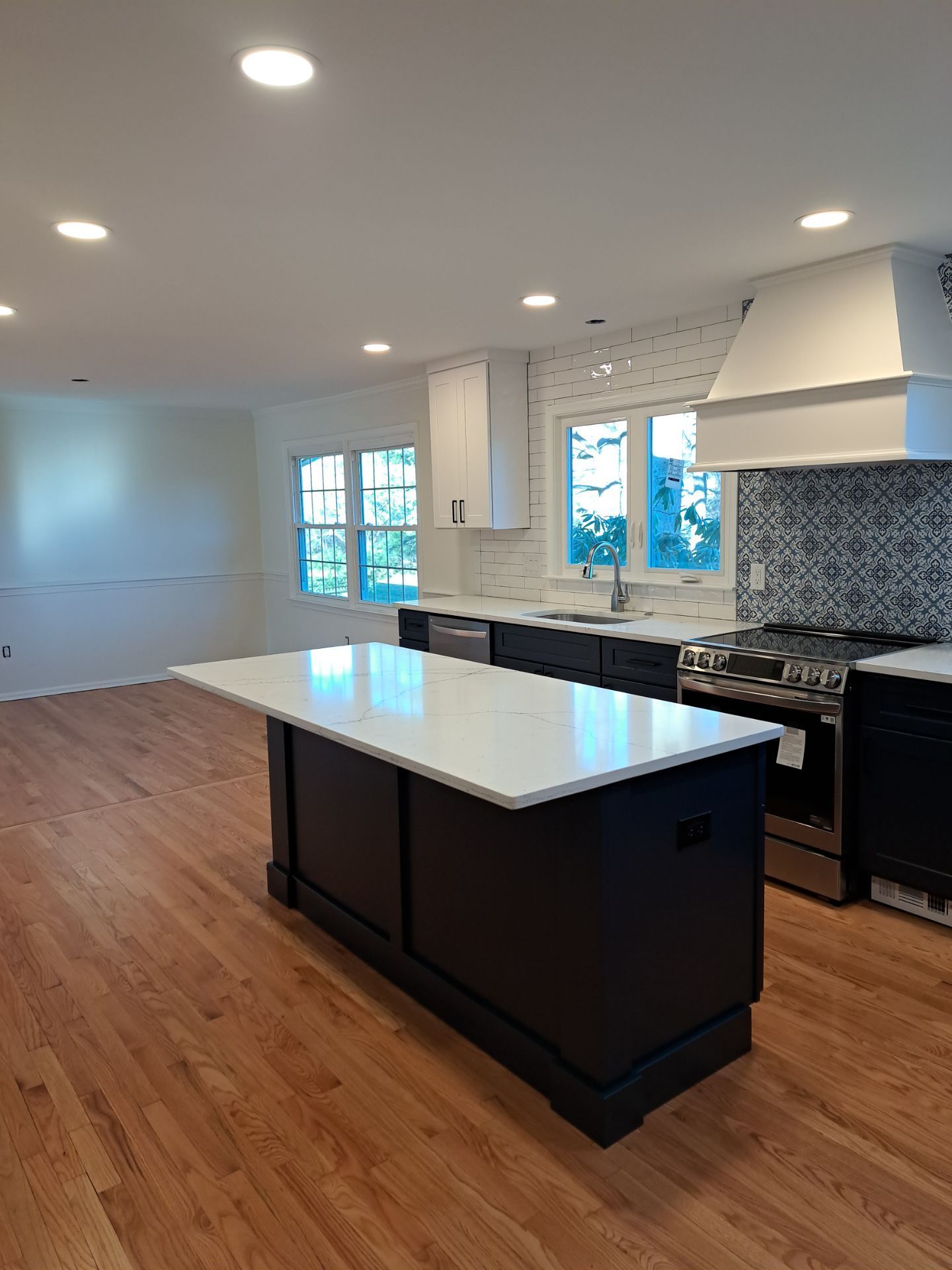 Kitchen with island, dark cabinets, white countertop, stainless steel appliances, and wood floor.