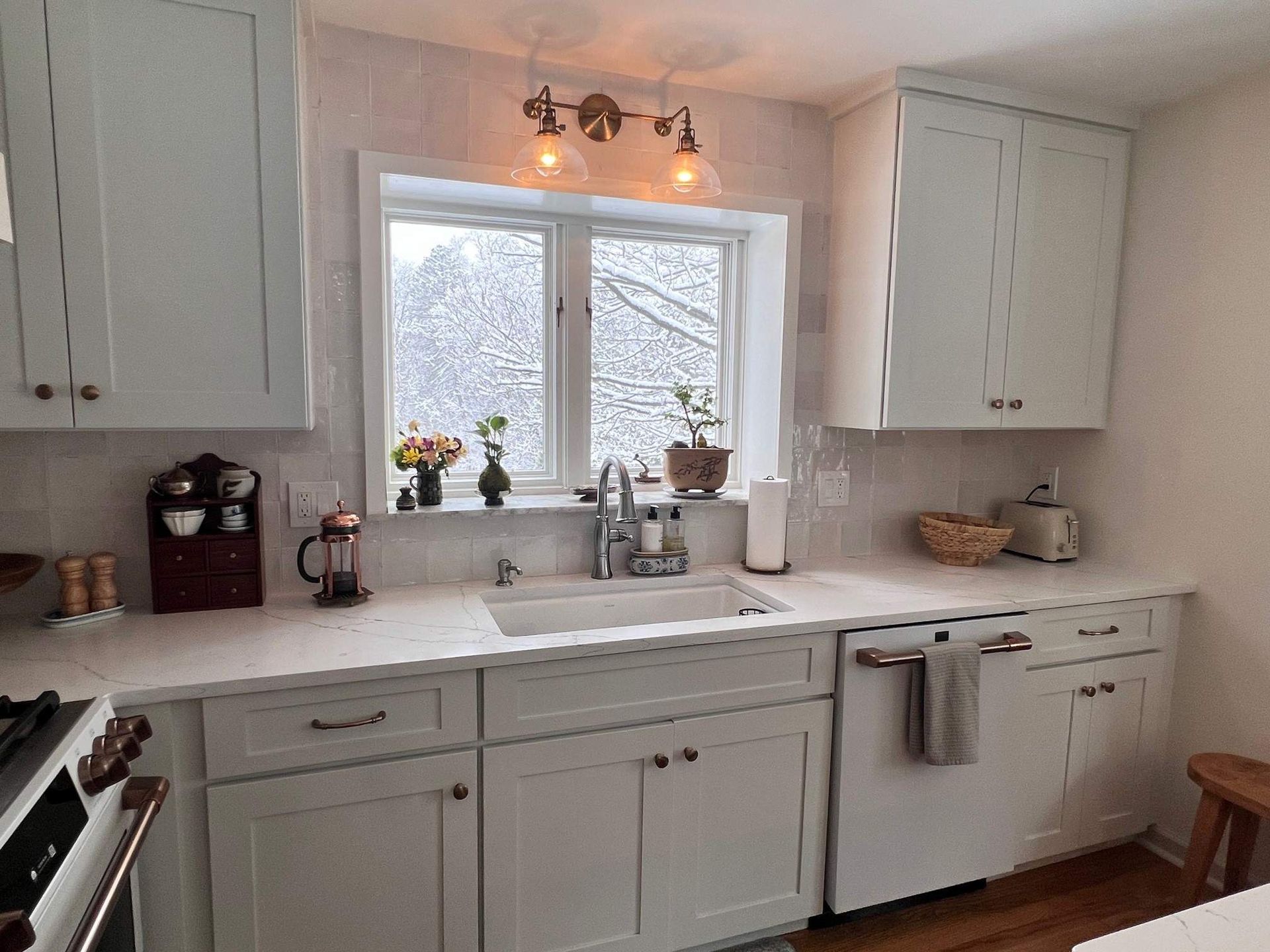 Kitchen with light blue cabinets, white countertops, and a window with a snowy view.