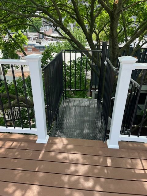 Deck with stairs leading down, black metal railing, and white posts. Tree branches overhead.