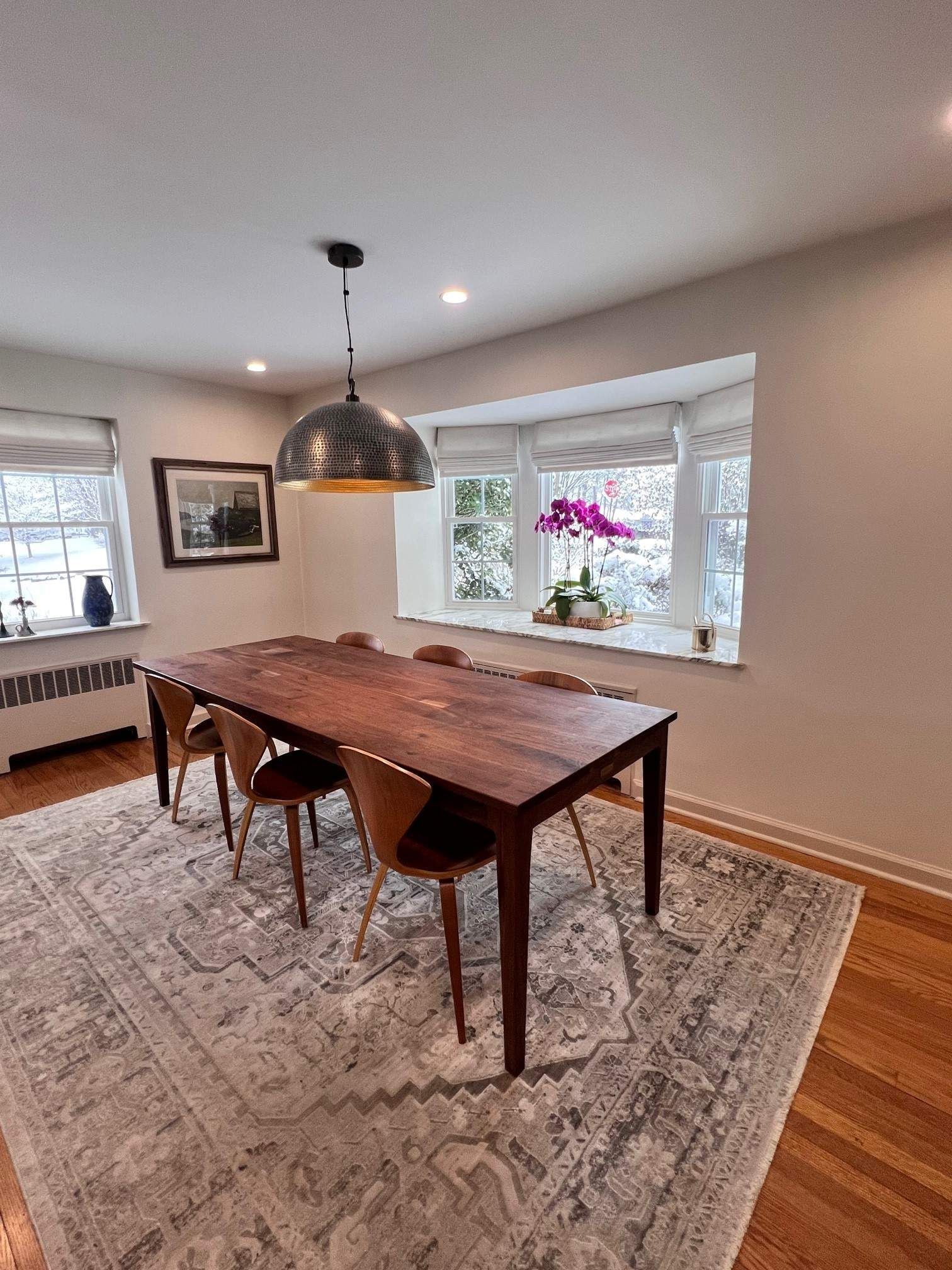 Dining room with wood table, modern chairs, patterned rug, and a bay window.