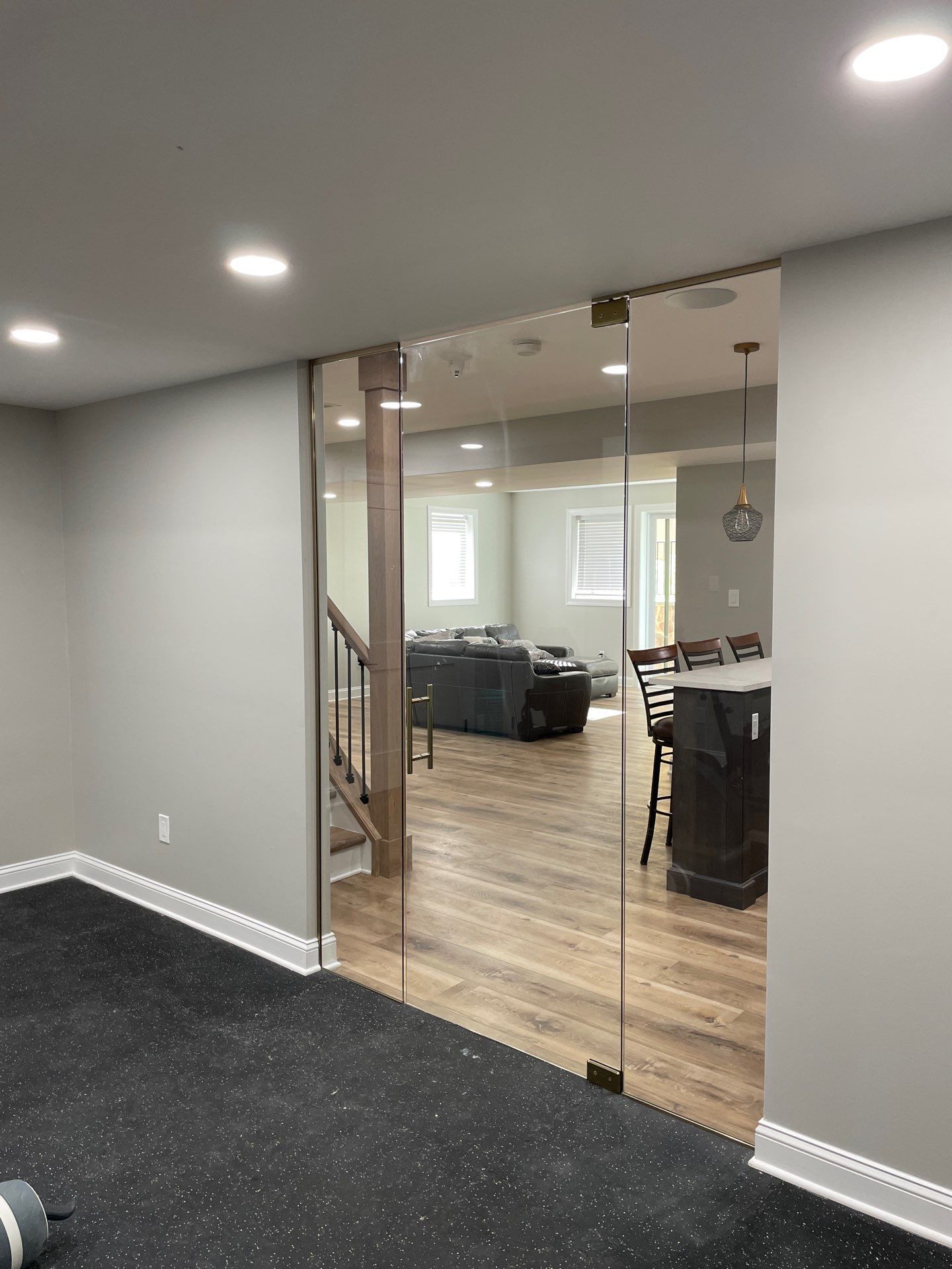 Glass door opening to a living area with wood flooring and gray walls. Black rubber flooring in the foreground.