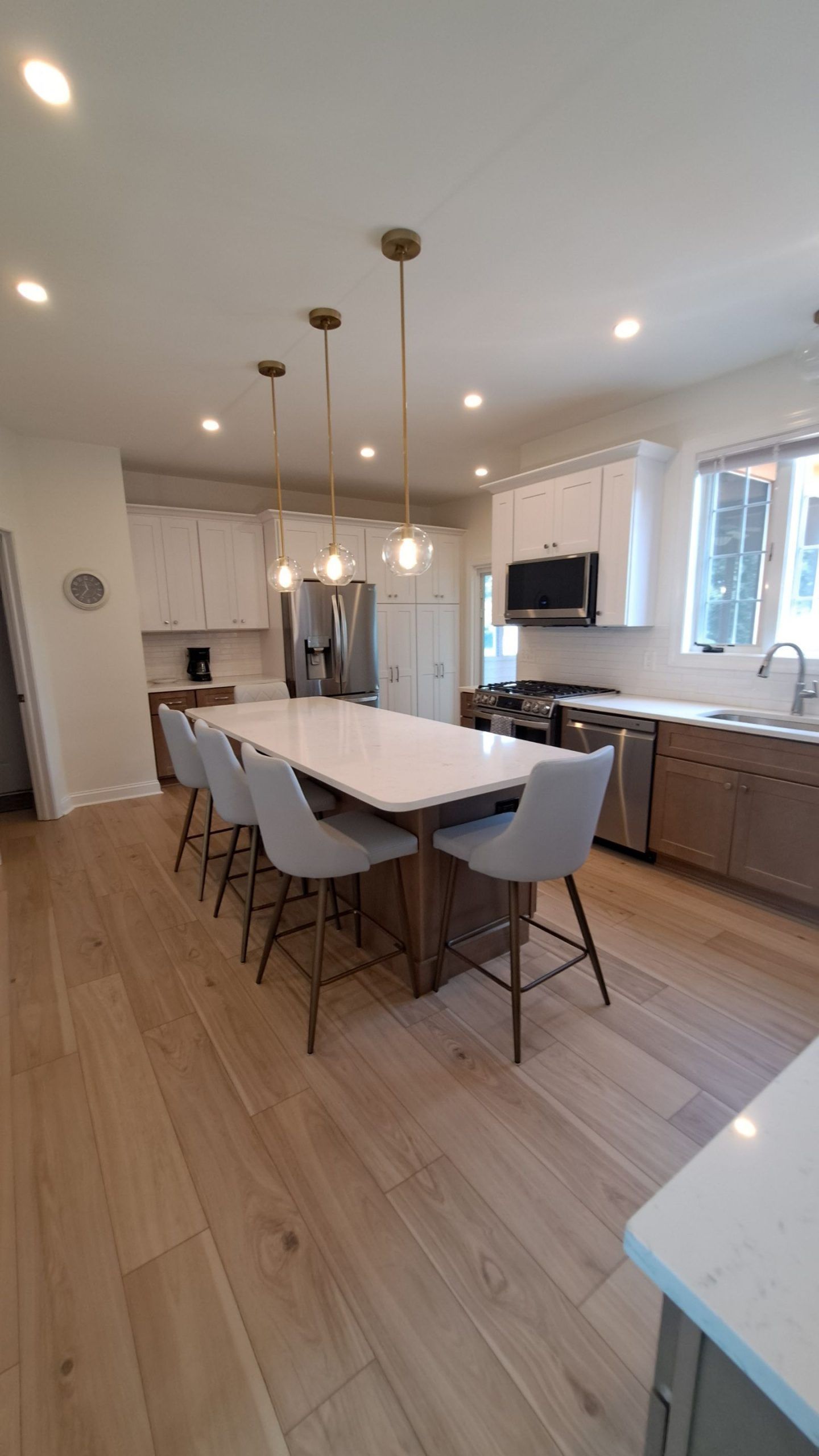 Modern kitchen with large island, seating, white cabinets, light wood floor, and pendant lights.