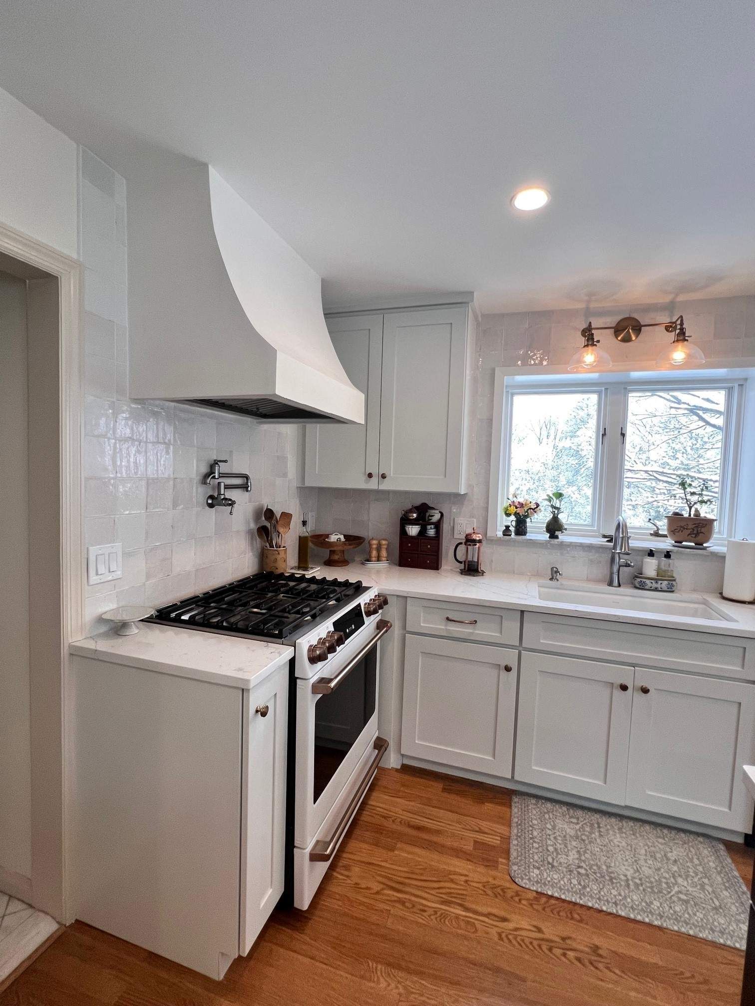 White kitchen with stove, cabinets, and a window overlooking greenery.