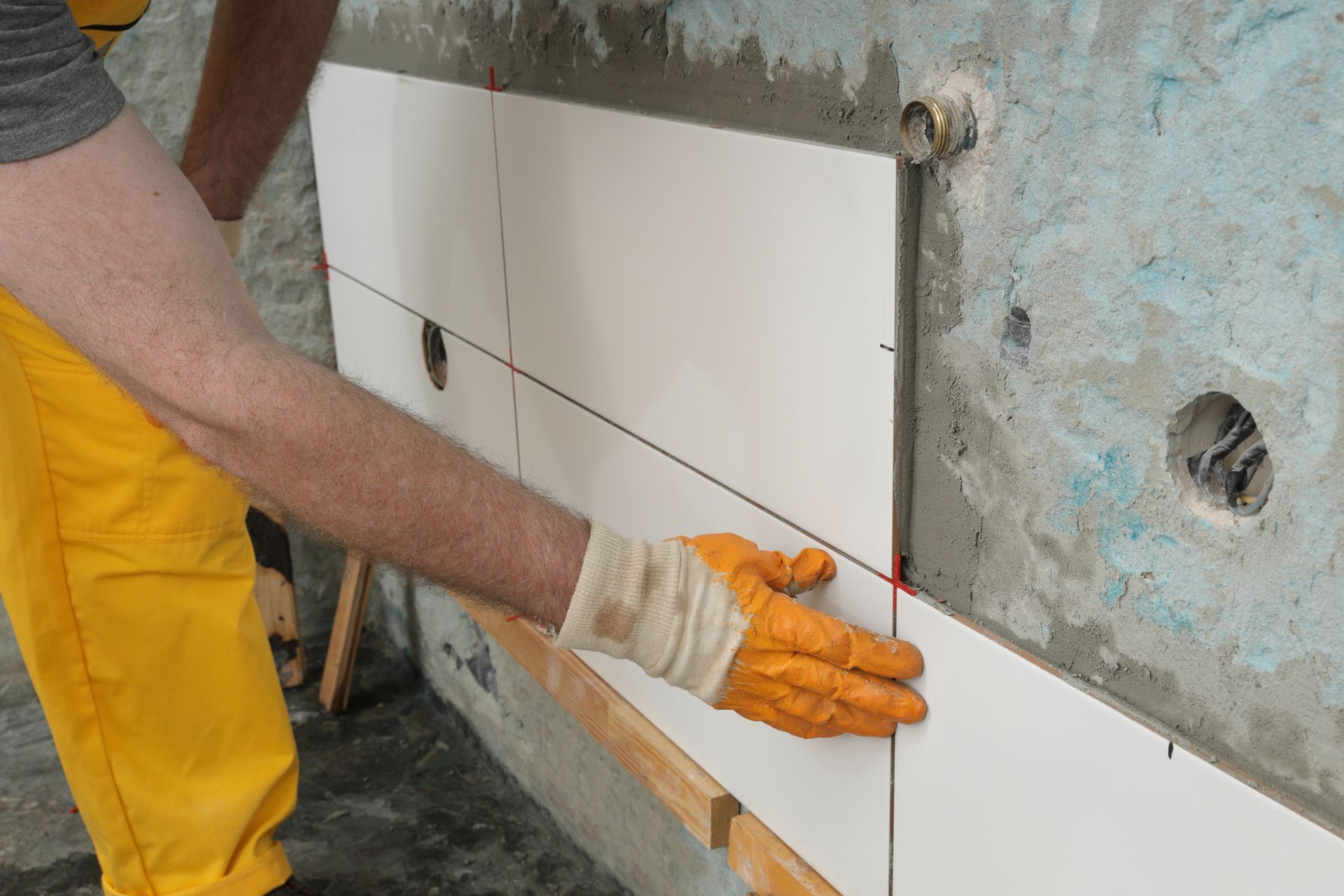 Close-up of a worker’s gloved hands as he places a ceramic tile on a concrete wall.