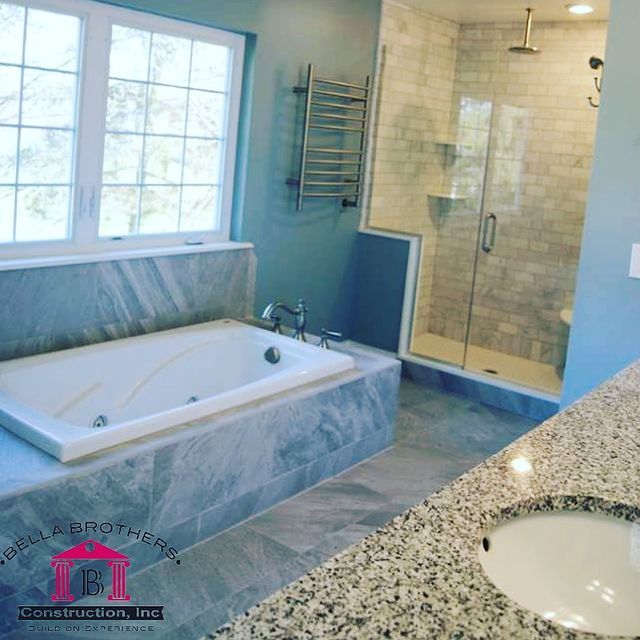 Bathroom with a tub, shower, and vanity. Gray tile and light blue walls.