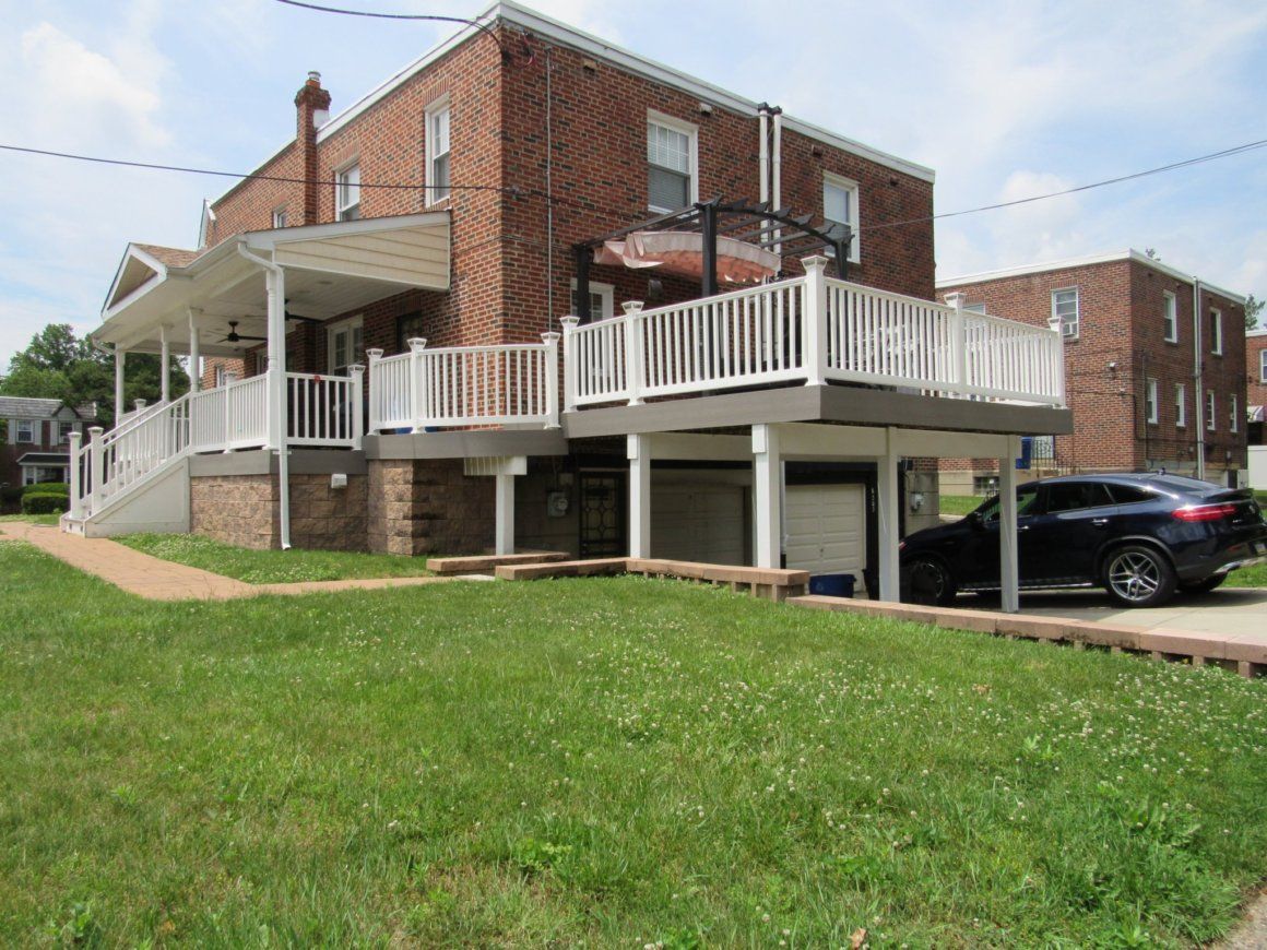 Brick house with a two-level deck, white railings, and a garage. Black car parked under deck.